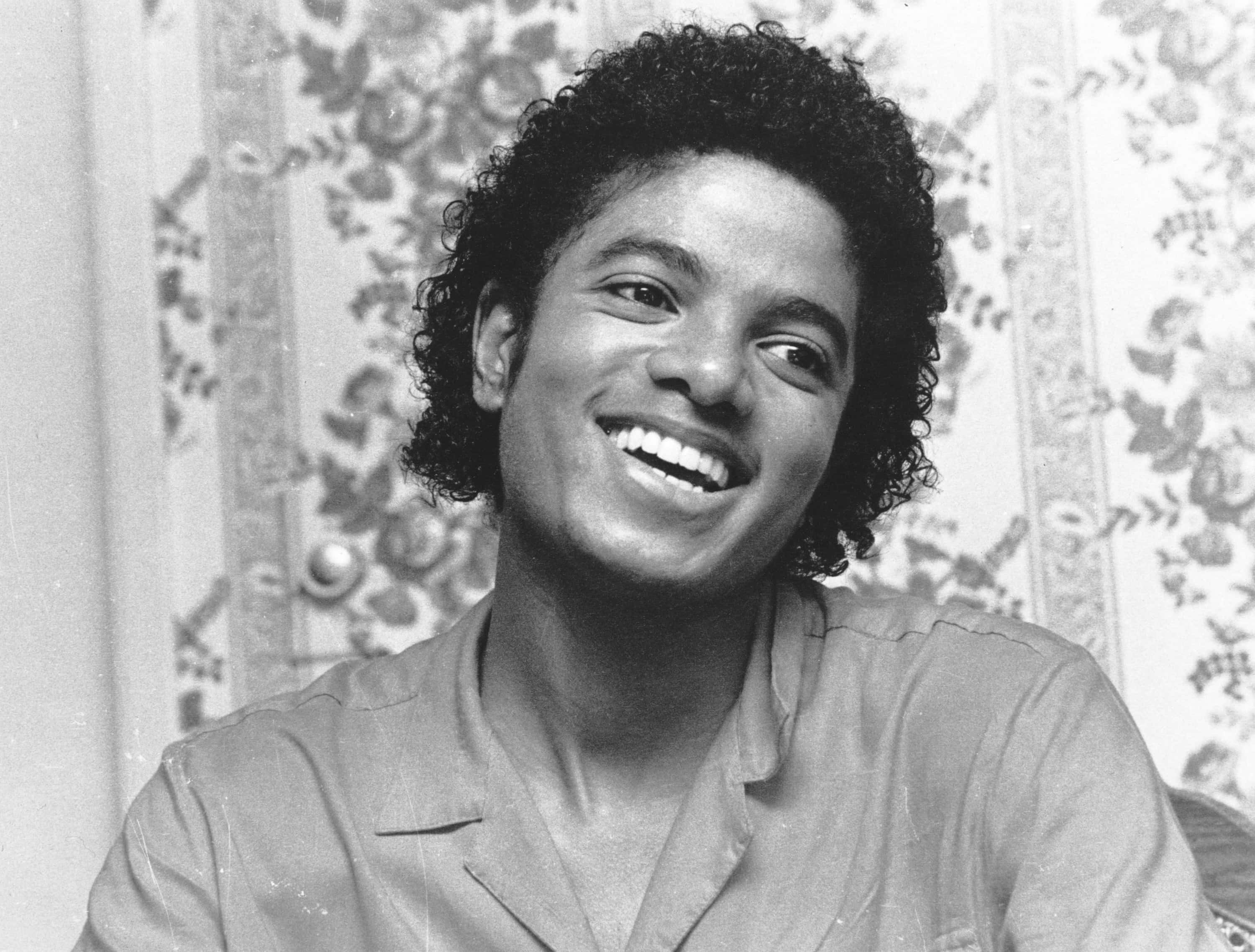 Young Michael Jackson 桌布 壁紙 — 一位快樂的捲髮年輕男子在復古花卉壁紙房間中燦爛地微笑。
