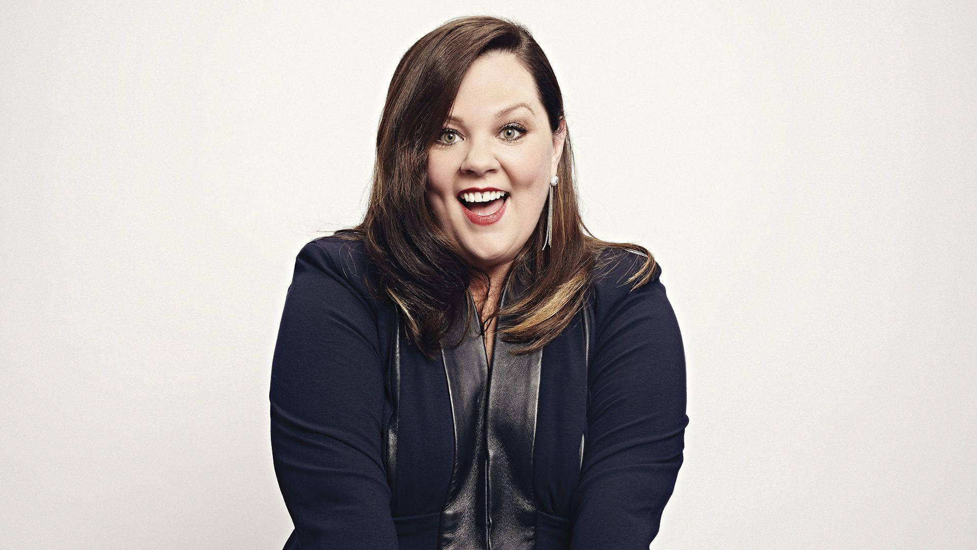 Celebrity 桌布 壁紙 — 一位快樂的棕髮女性，帶著燦爛的笑容，穿著深藍色外套，背景是純白色。