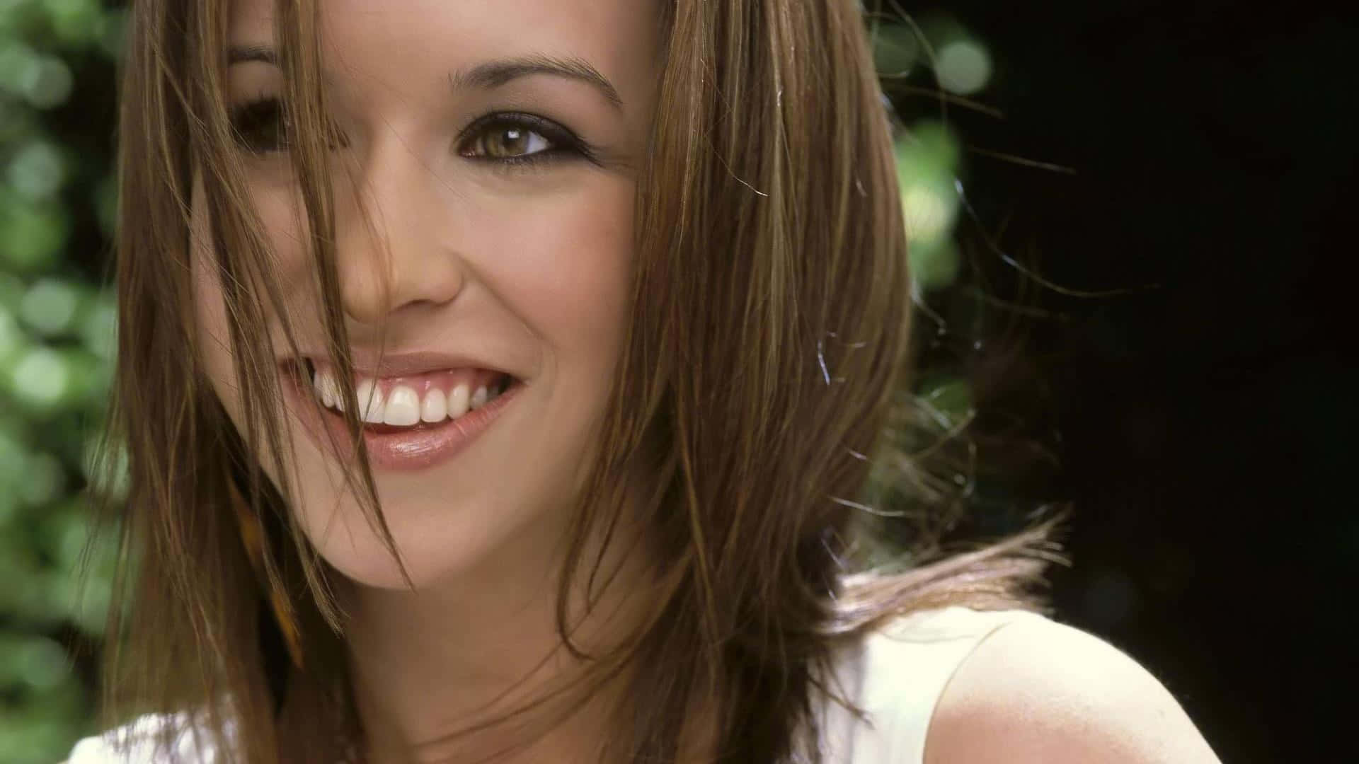 lacey chabert 桌布 壁紙 — 一位快樂的棕髮女性在柔和的綠色模糊背景前，髮絲飄過臉龐，露出燦爛的笑容。