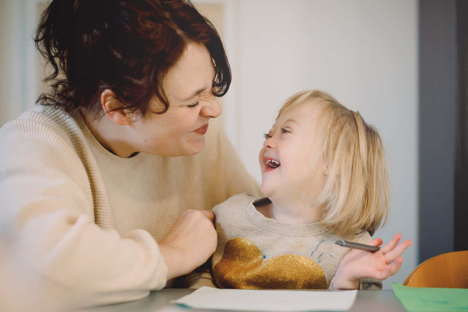 Mother Love 桌布 壁紙 — 一位快樂的母親和她大笑的幼兒在室內分享溫馨時刻，彼此燦爛地微笑。