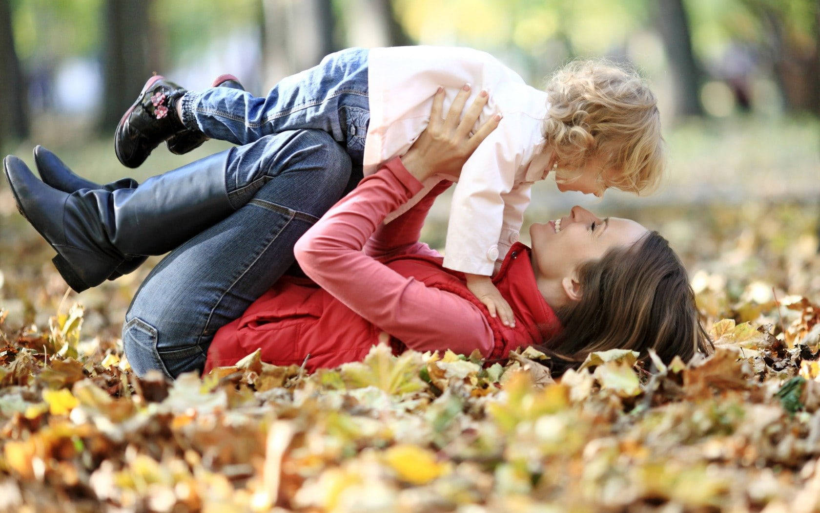 Family 桌布 壁紙 — 一位快樂的母親和幼兒在陽光普照的公園裡，在金黃色的秋葉地毯上分享嬉戲的時刻。