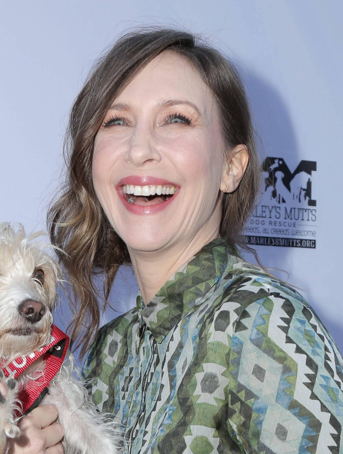 Celebrity 桌布 壁紙 — 一位快樂的波浪棕色頭髮女性在Marley's Mutts活動中抱著一隻白色毛茸茸的小狗，開懷大笑。
