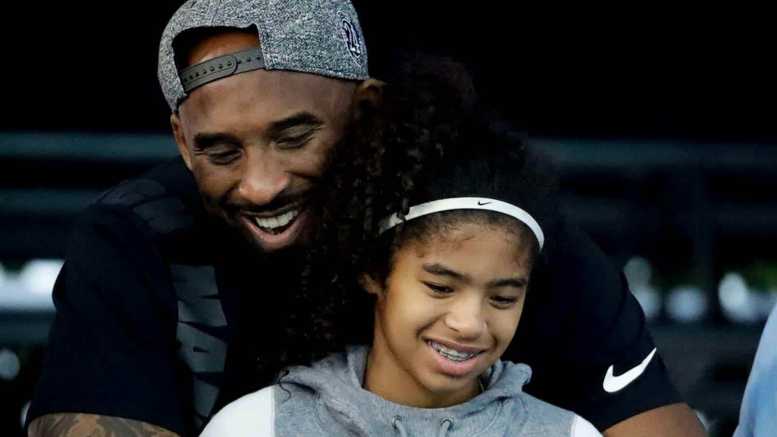 Kobe And Gigi 桌布 壁紙 — 一位快樂的父親和女兒在昏暗的燈光下分享溫暖的擁抱和燦爛的笑容。