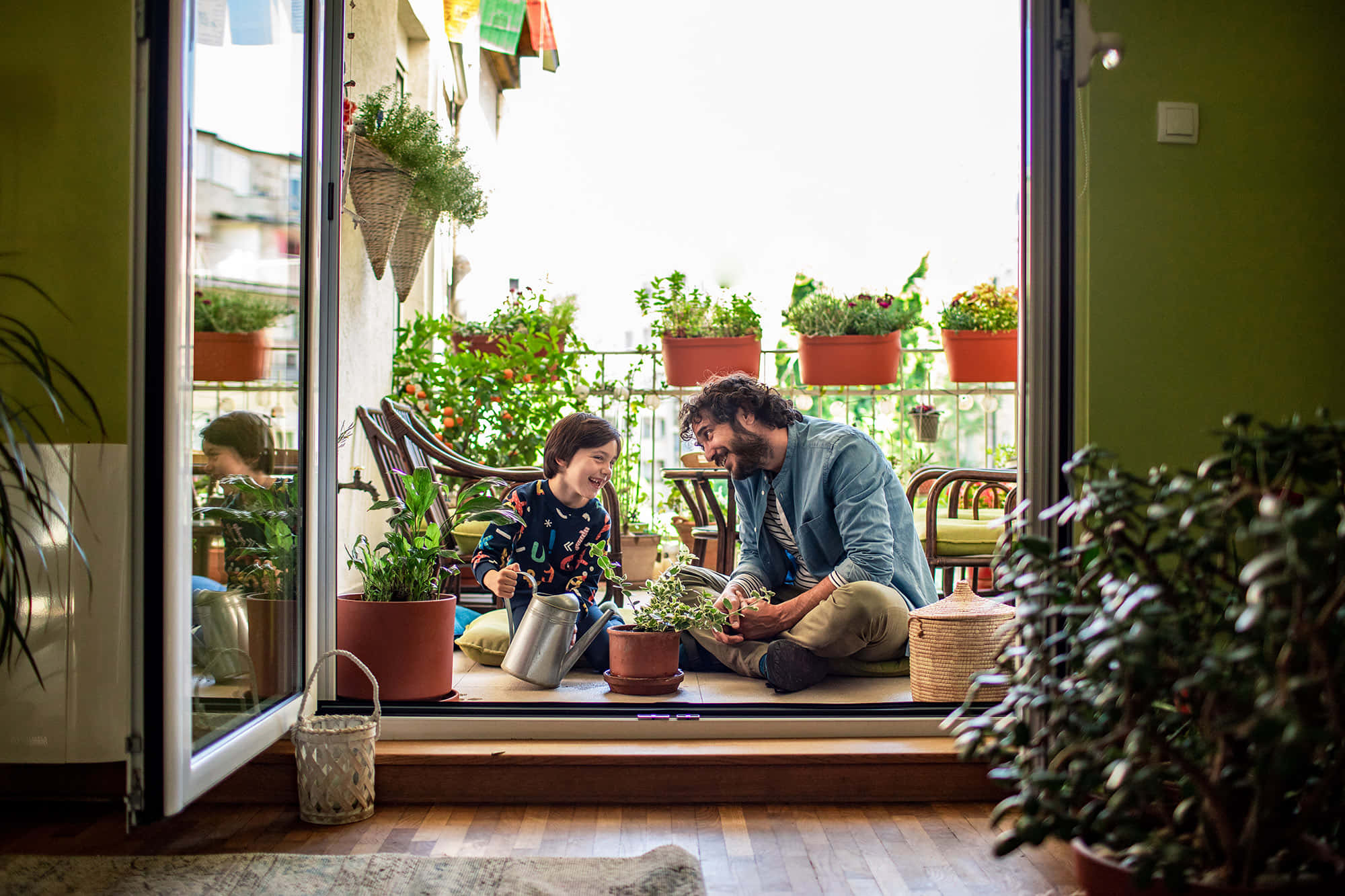 Gardening 桌布 壁紙 — 一位快樂的父親和孩子在陽光普照、綠意盎然的陽台上照料盆栽時開懷大笑。