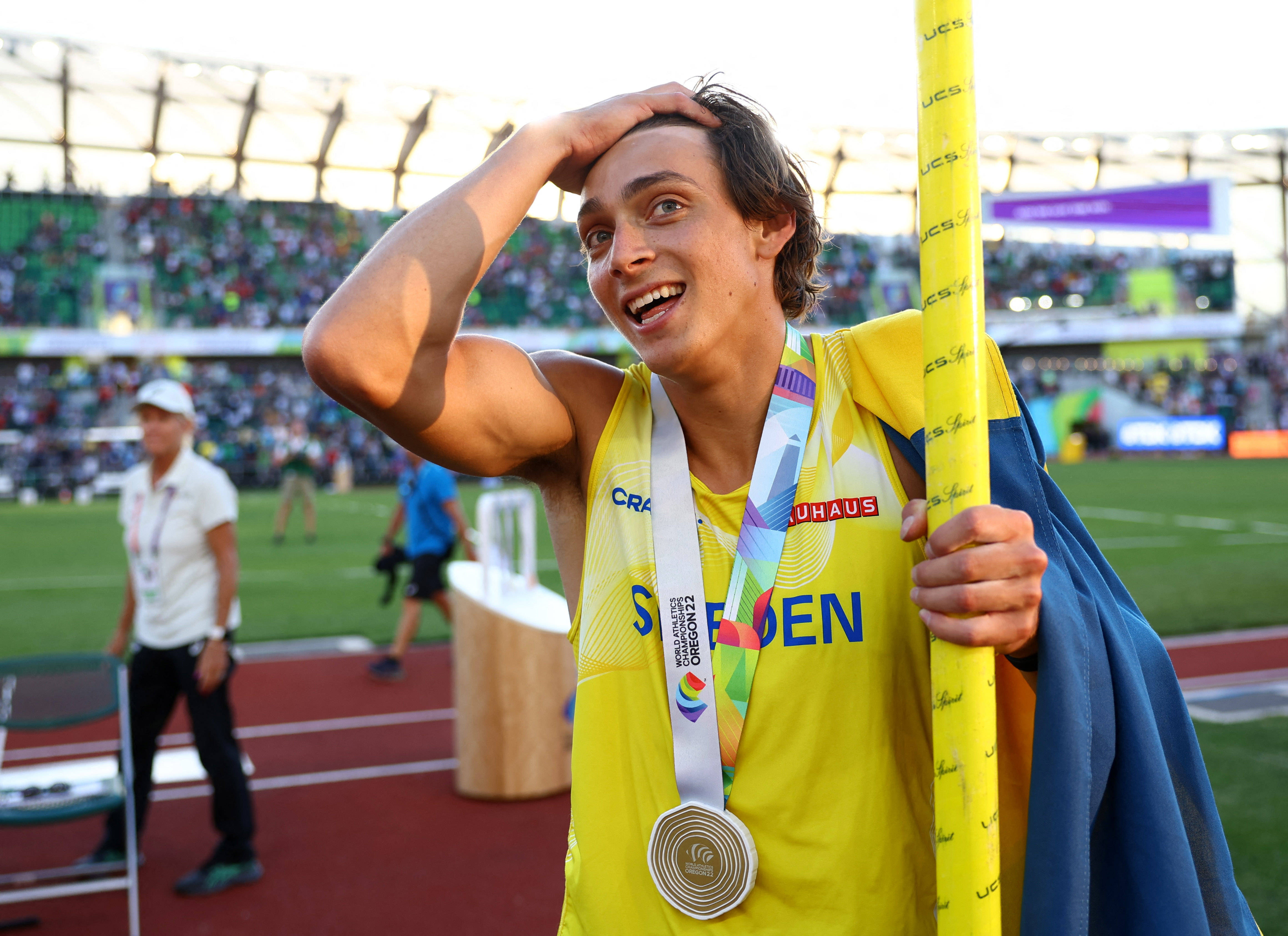 Athletic 桌布 壁紙 — 一位快樂的瑞典撐竿跳運動員在日落時分的體育場內，手持金牌和旗幟慶祝。