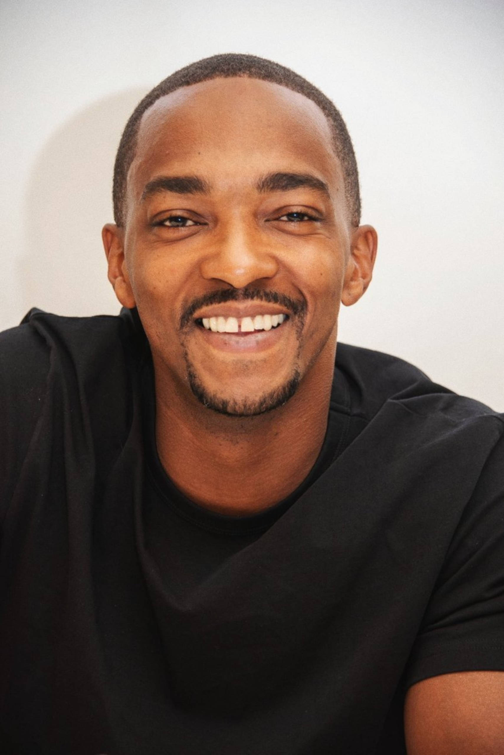 Anthony Mackie 桌布 壁紙 — 一位快樂的男子，帶著溫暖的笑容和整齊修剪的鬍鬚，穿著黑色T恤，背景是純白色。