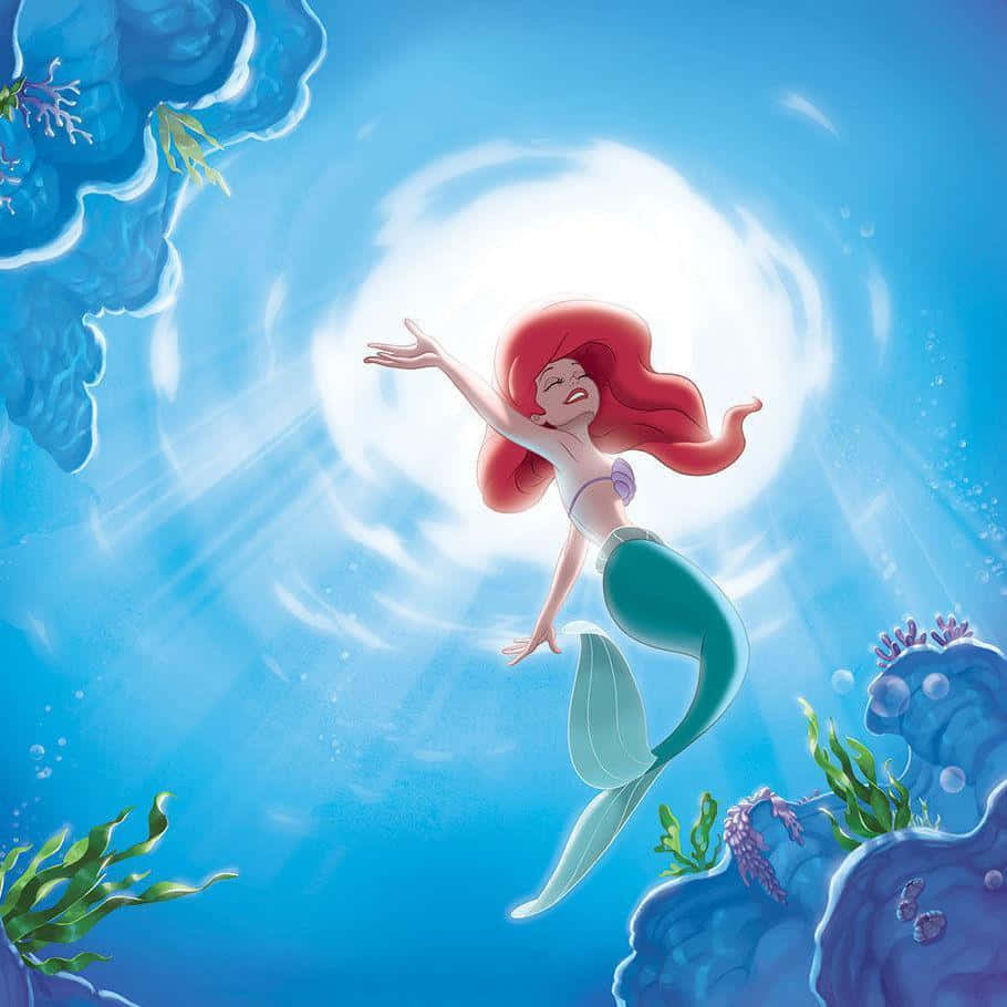 little mermaid 桌布 壁紙 — 一位快樂的美人魚，擁有飄逸的紅髮，在陽光照耀的藍色海水中向上游，周圍環繞著珊瑚和海藻。