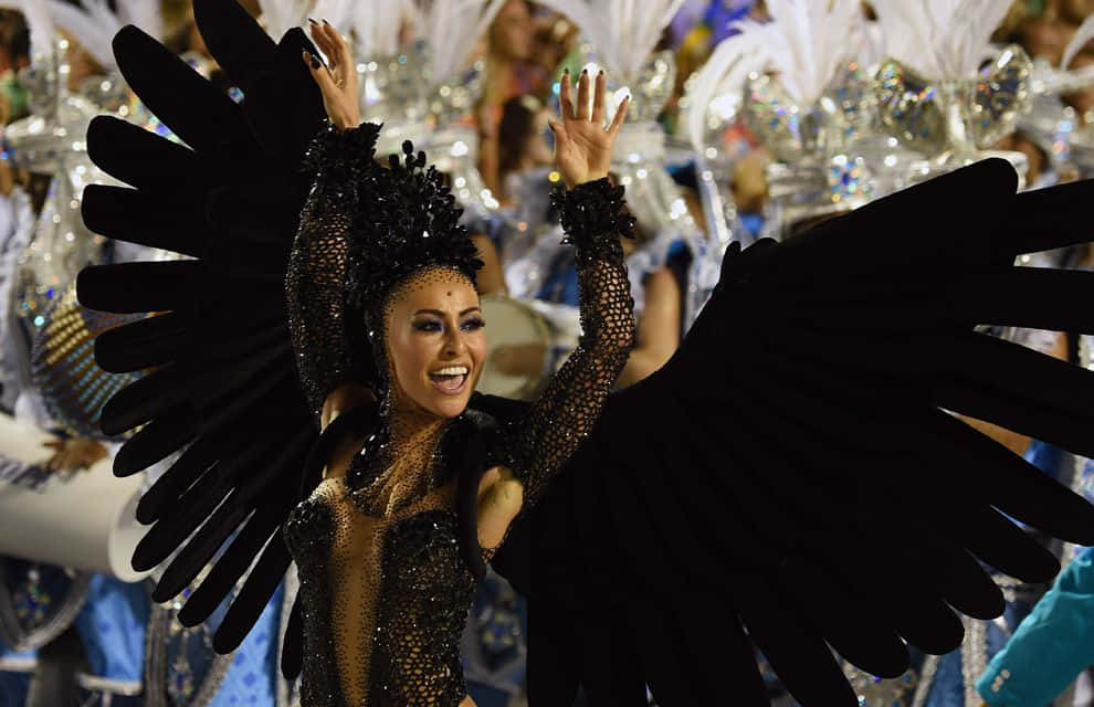 Carnival 桌布 壁紙 — 一位快樂的舞者穿著黑色羽毛服裝，展開翅膀，在充滿活力的嘉年華遊行中燦爛微笑。