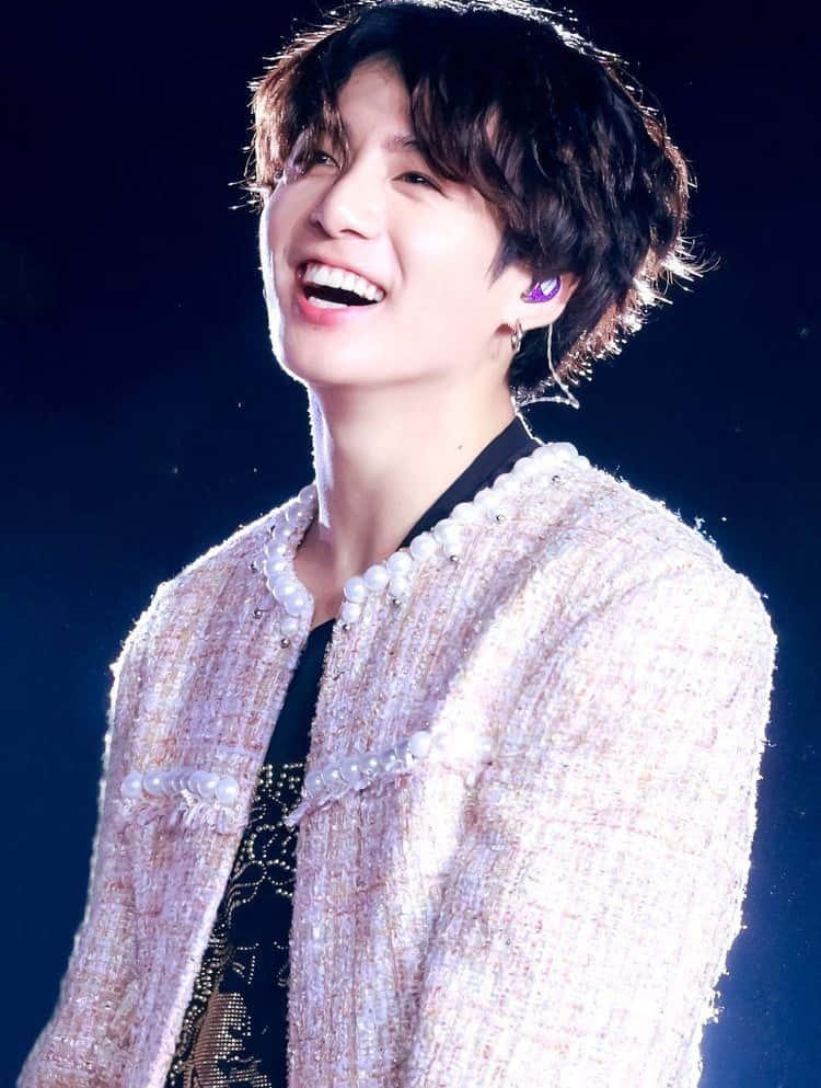 Jungkook 桌布 壁紙 — 一位快樂的表演者穿著珍珠裝飾的夾克，在黑暗背景的舞台燈光下燦爛微笑。