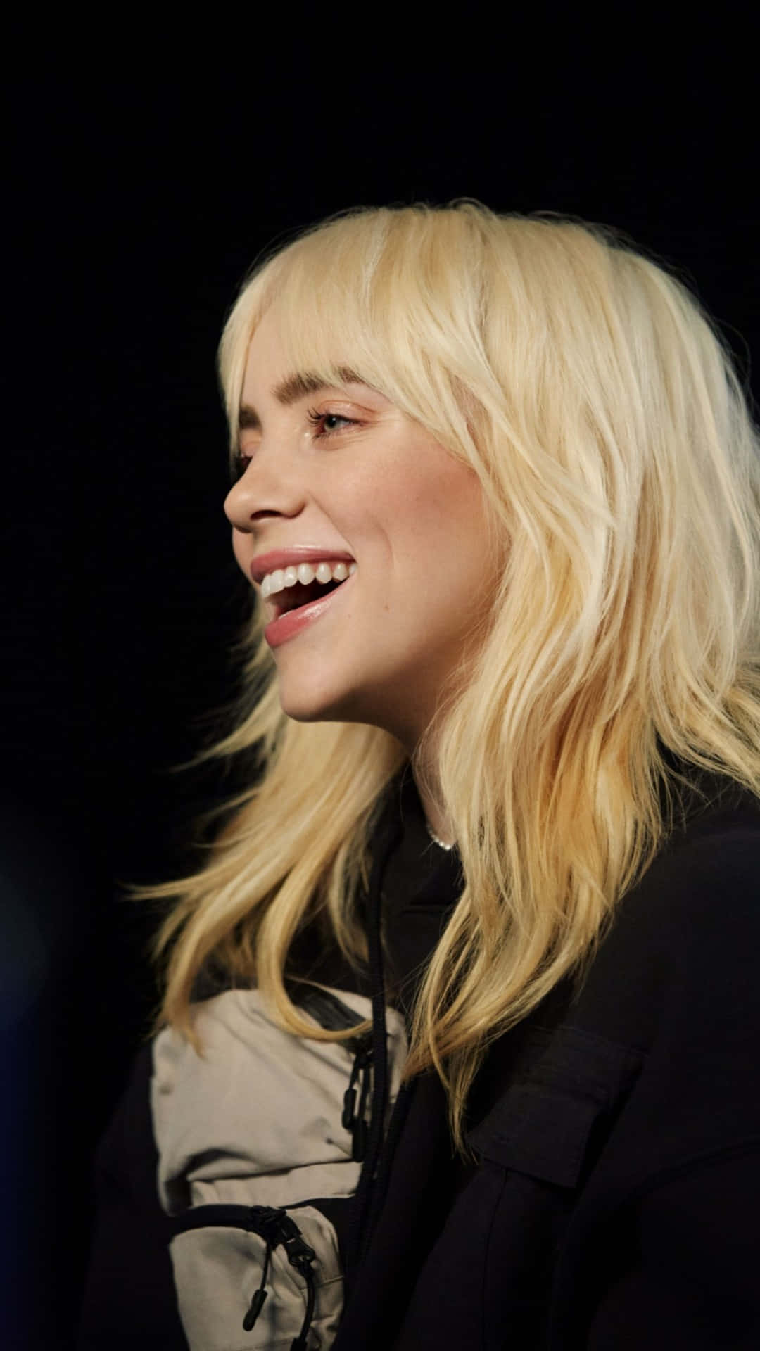 Billie Eilish 2021 桌布 壁紙 — 一位快樂的金髮女性在純黑背景下燦爛大笑，頭髮自然垂落。