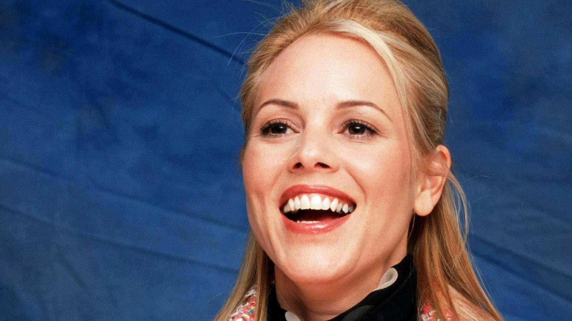 Actress HD 桌布 壁紙 — 一位快樂的金髮女郎在溫暖燈光下，對著有紋理的藍色背景燦爛大笑。