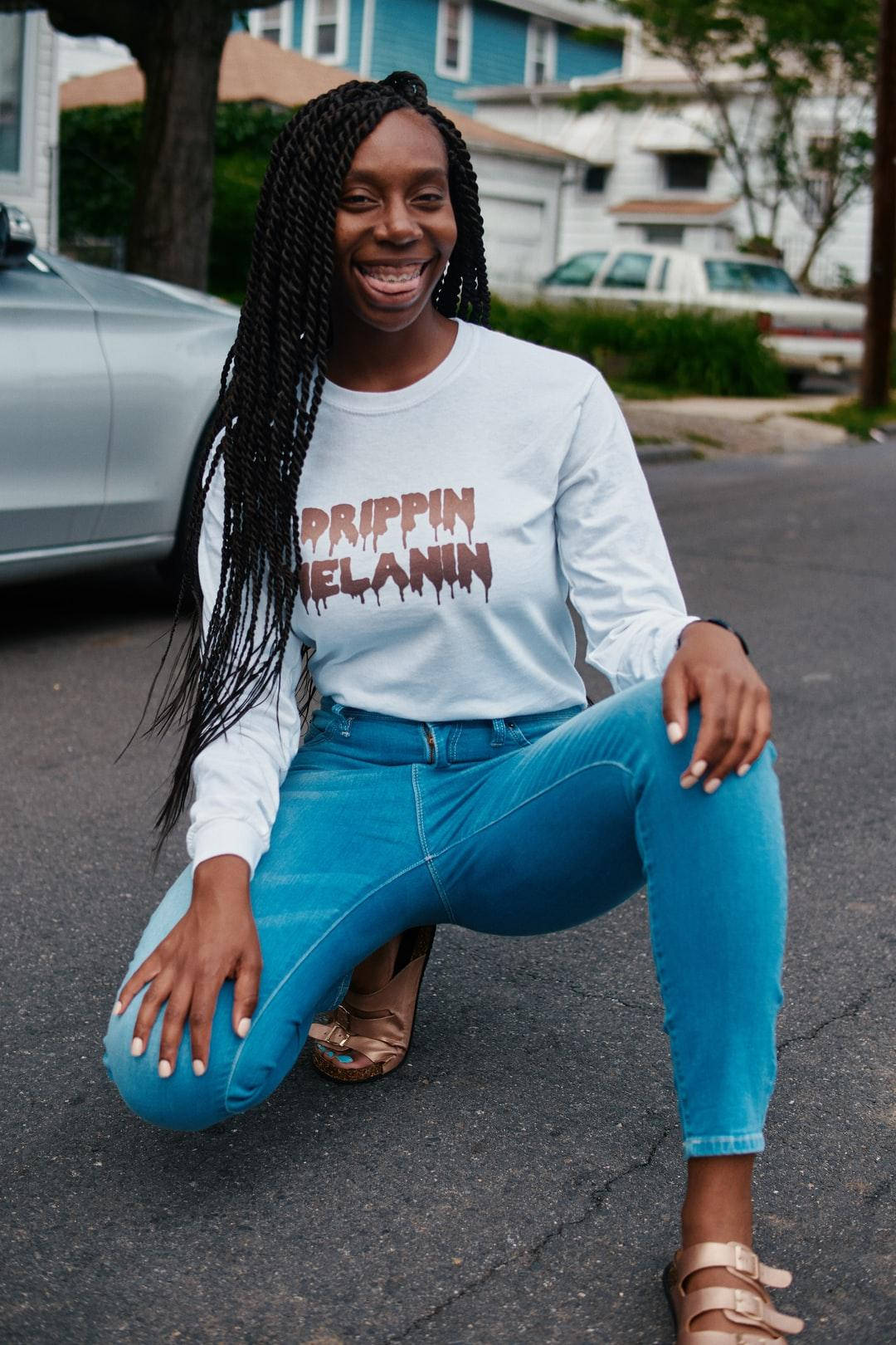 女士蹲在街上，穿著 'Prippin Melanin' 襯衫和藍色牛仔褲。 — 壞女孩 GIF 壁紙