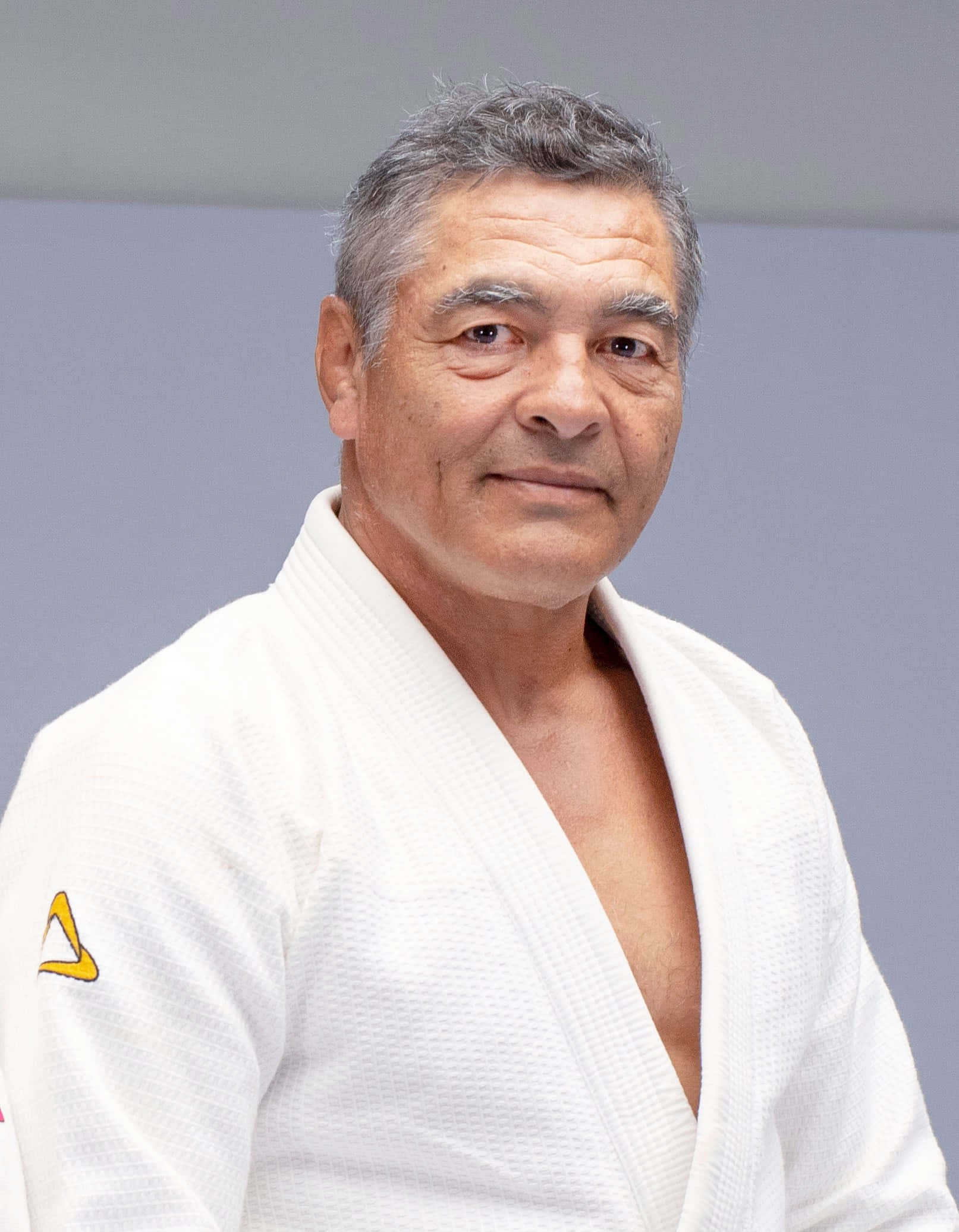 martial arts 桌布 壁紙 — 一位成熟的白髮男士穿著白色柔道服，背景為純灰色，袖子上有一個微妙的黃色標誌。