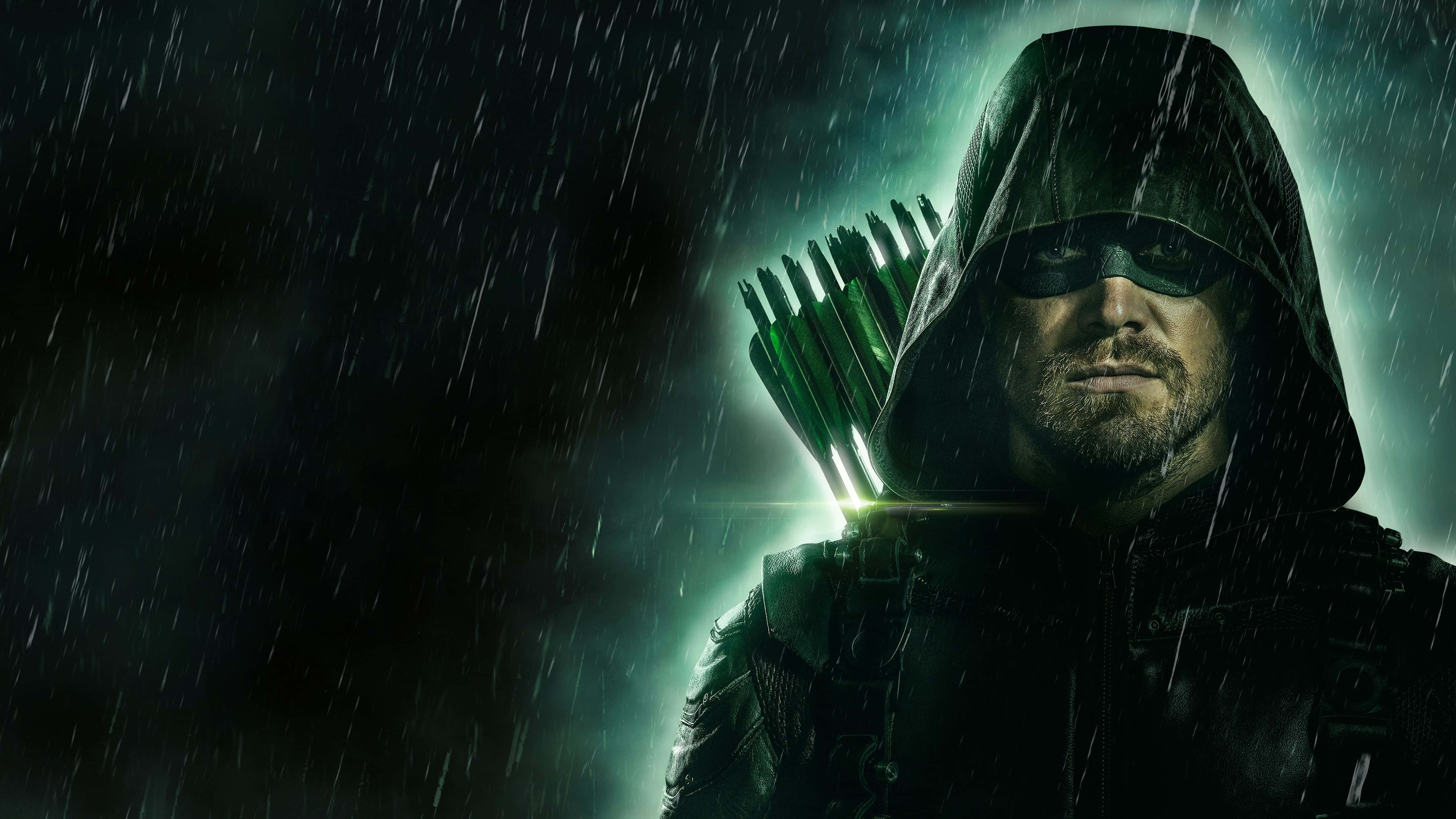 Green Arrow 桌布 壁紙 — 一位戴兜帽的弓箭手站在雨中，手持發光的綠色箭矢，背景是黑暗的暴風雨。