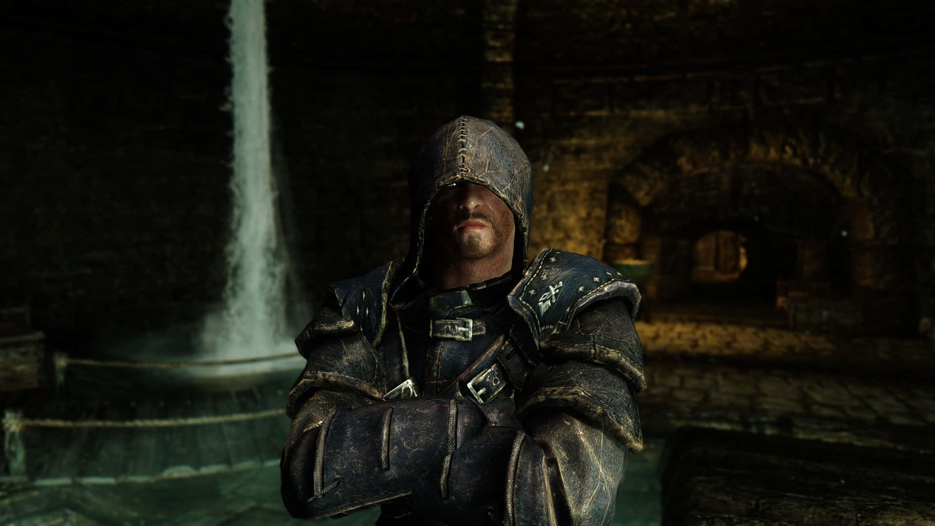 Skyrim Brynjolf 桌布 壁紙 — 一位戴兜帽的裝甲戰士在昏暗的石室中，雙臂交叉站在瀑布旁。