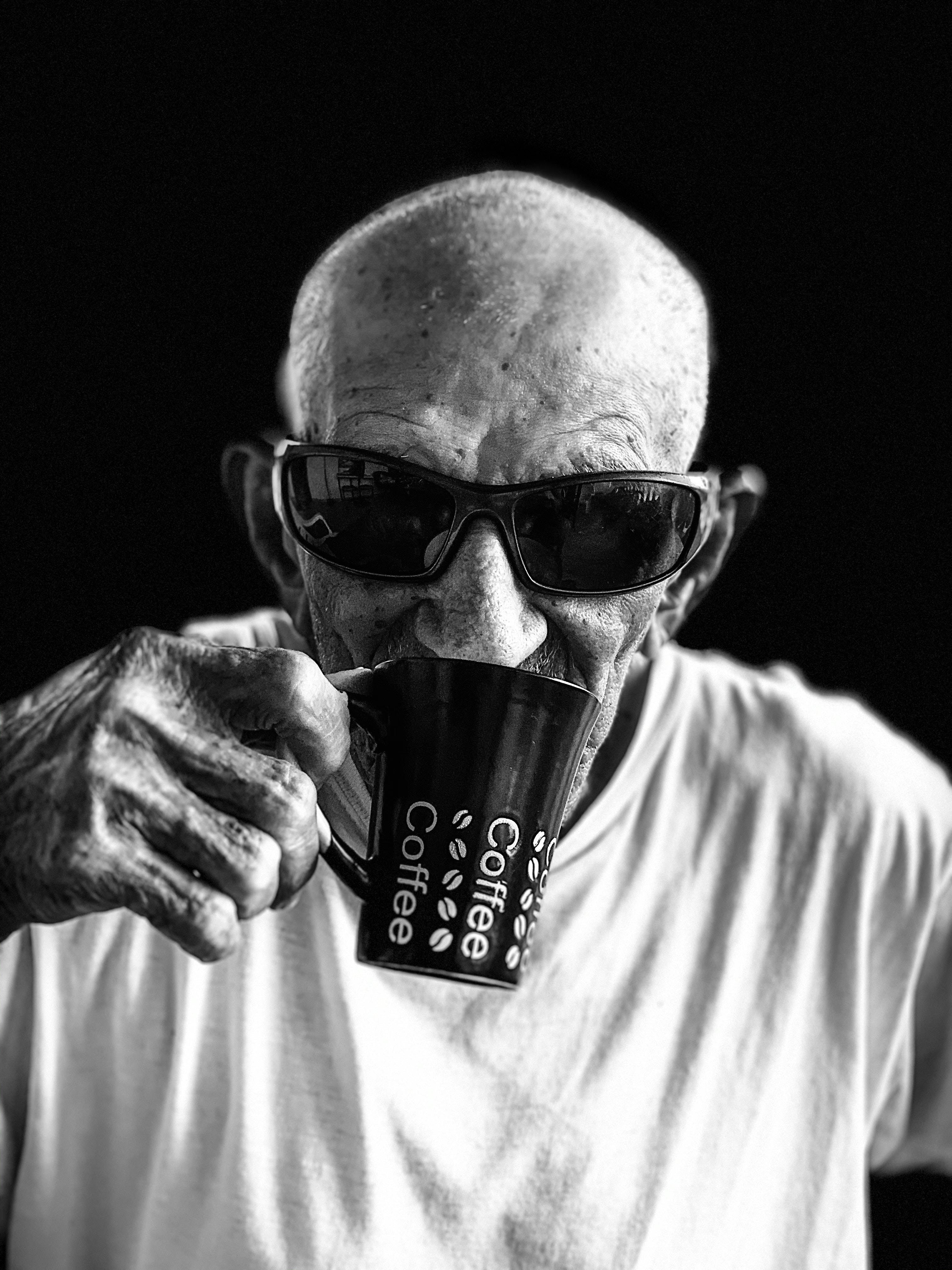 Drinking 桌布 壁紙 — 一位戴太陽眼鏡的長者男士在深色背景前喝咖啡的黑白肖像。
