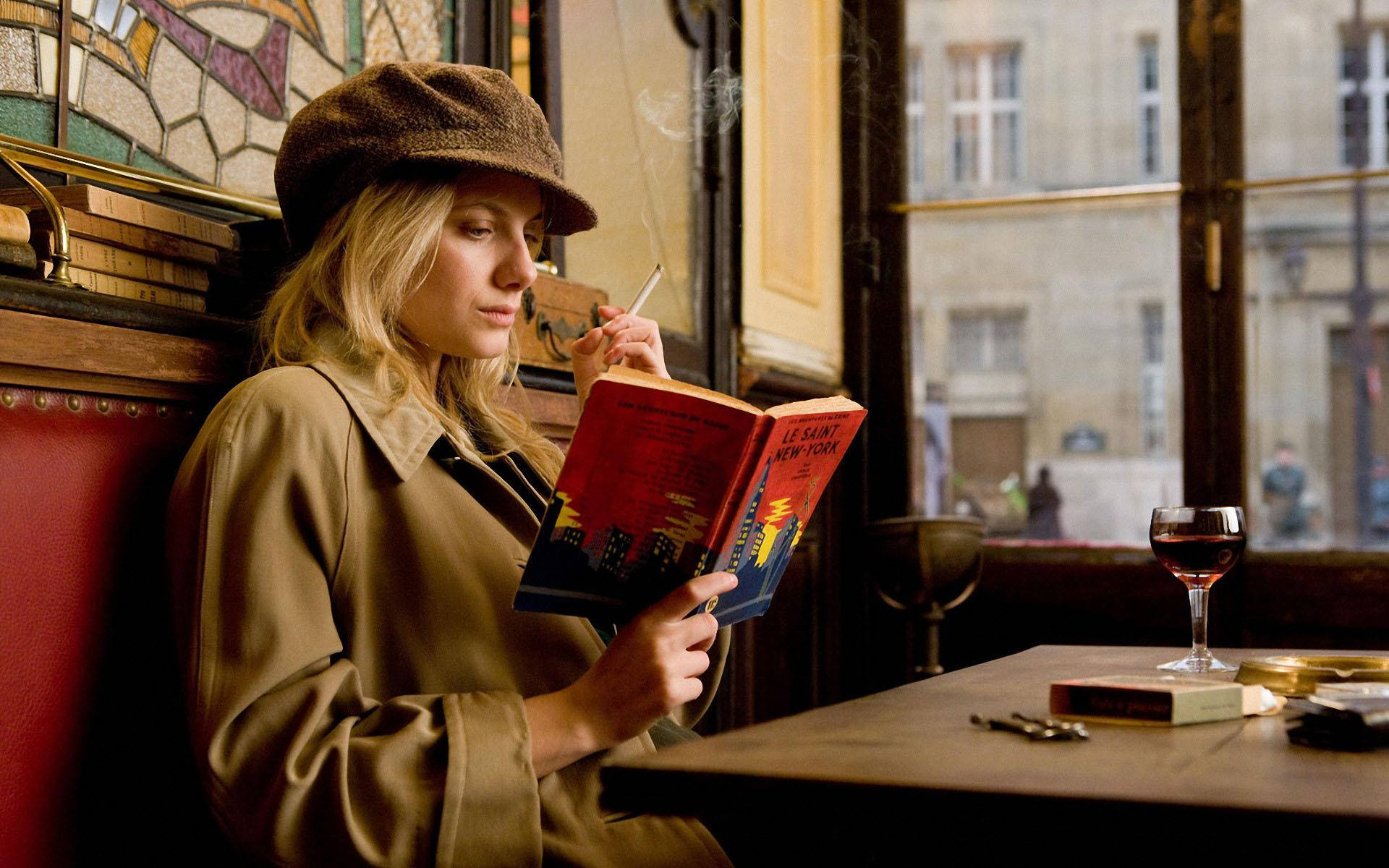Inglourious Basterds 桌布 壁紙 — 一位戴棕色帽子和穿棕色外套的女性，在舒適的巴黎咖啡館裡，一邊抽煙一邊閱讀一本紅色的書，咖啡館內有彩繪玻璃和葡萄酒。