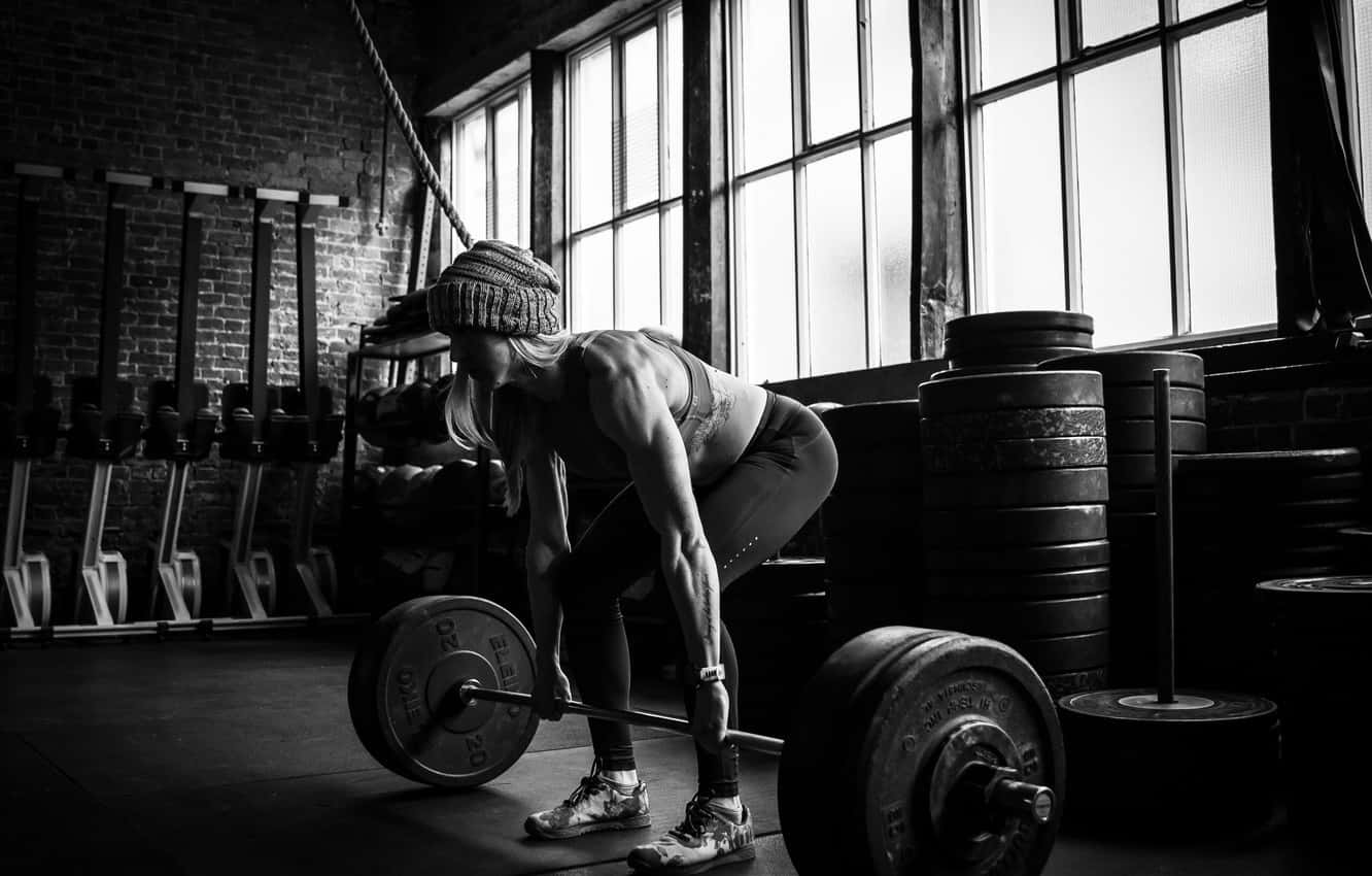 Exercise 桌布 壁紙 — 一位戴毛帽的女性在一個有磚牆和大窗戶的黑白健身房中舉起槓鈴。