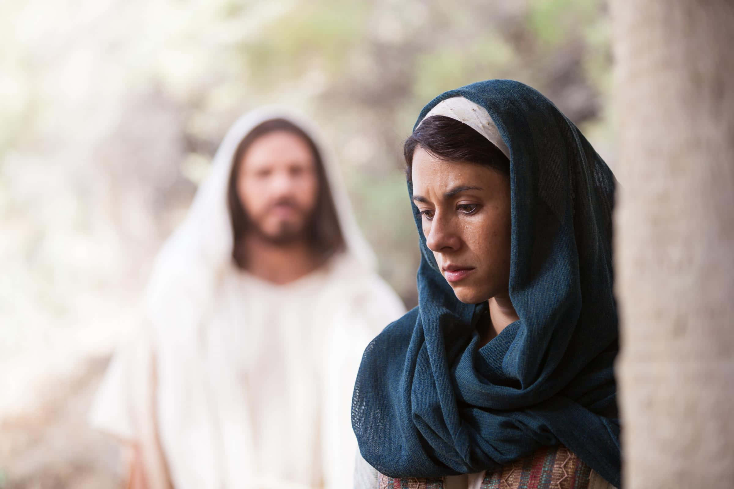 Mary Magdalene 桌布 壁紙 — 一位戴深藍色頭巾的女人靠在樹上，臉上刻滿悲傷，而一位穿白袍的男人模糊地站在背景中。