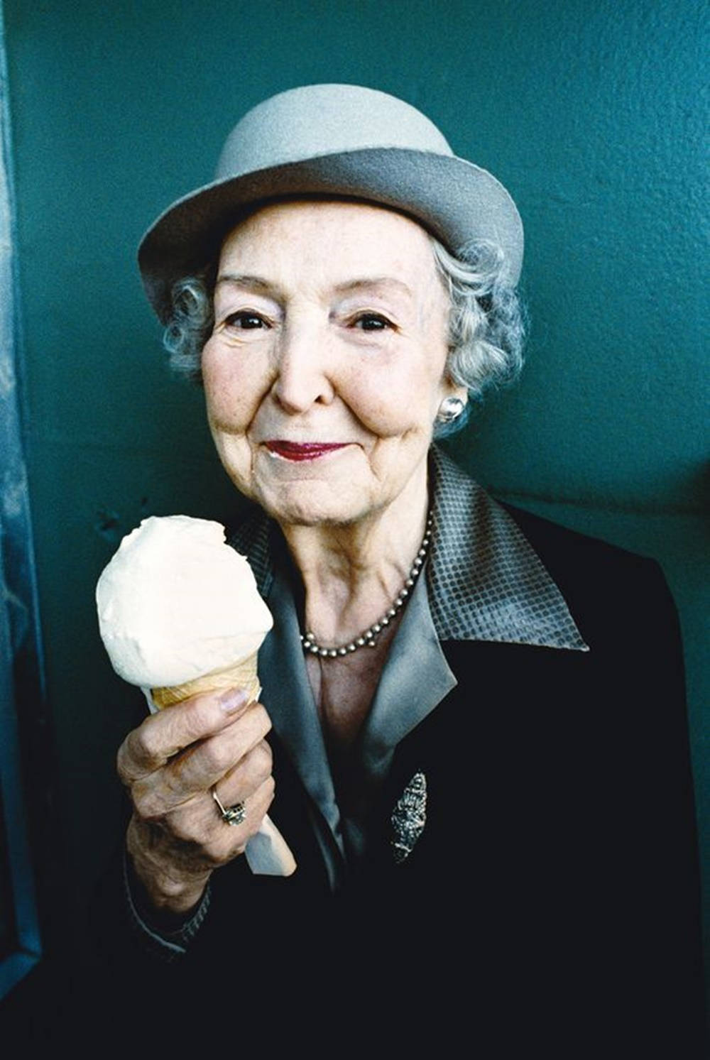 Grandma 桌布 壁紙 — 一位戴灰色帽子的老婦人，在青綠色牆壁前拿著一個香草冰淇淋甜筒，露出溫暖的笑容。