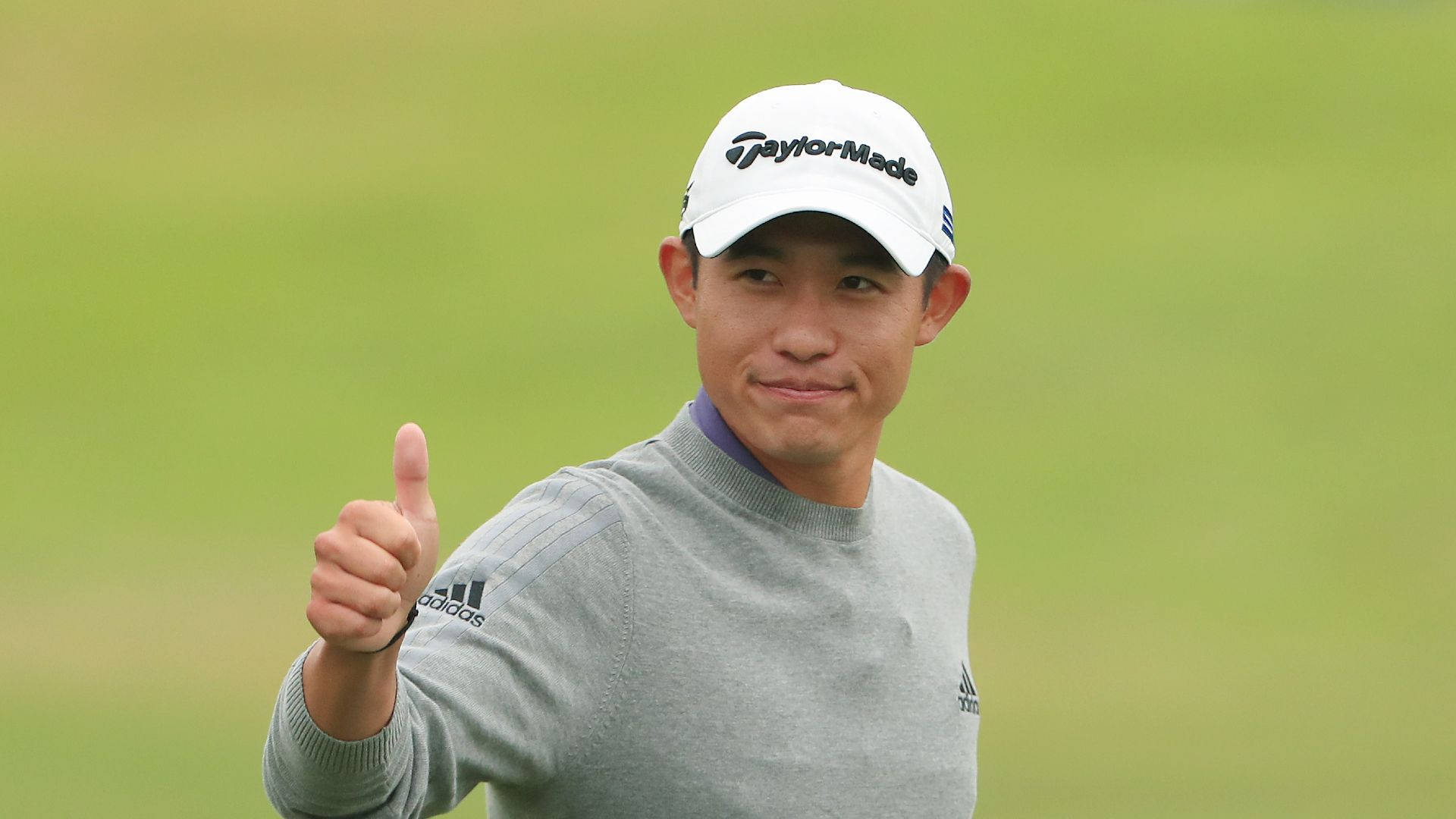 Pga 桌布 壁紙 — 一位戴白色帽子和灰色毛衣的高爾夫球手在翠綠的球場上自信地豎起大拇指微笑。