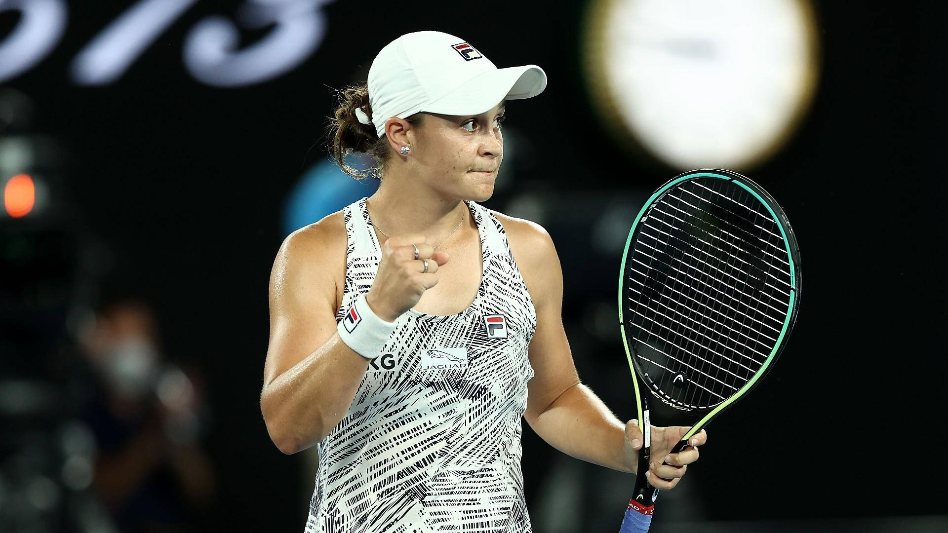 Ashleigh Barty 桌布 壁紙 — 一位戴白色帽子和穿圖案服裝的女網球選手，在體育館燈光下高舉拳頭慶祝勝利，同時握著球拍。