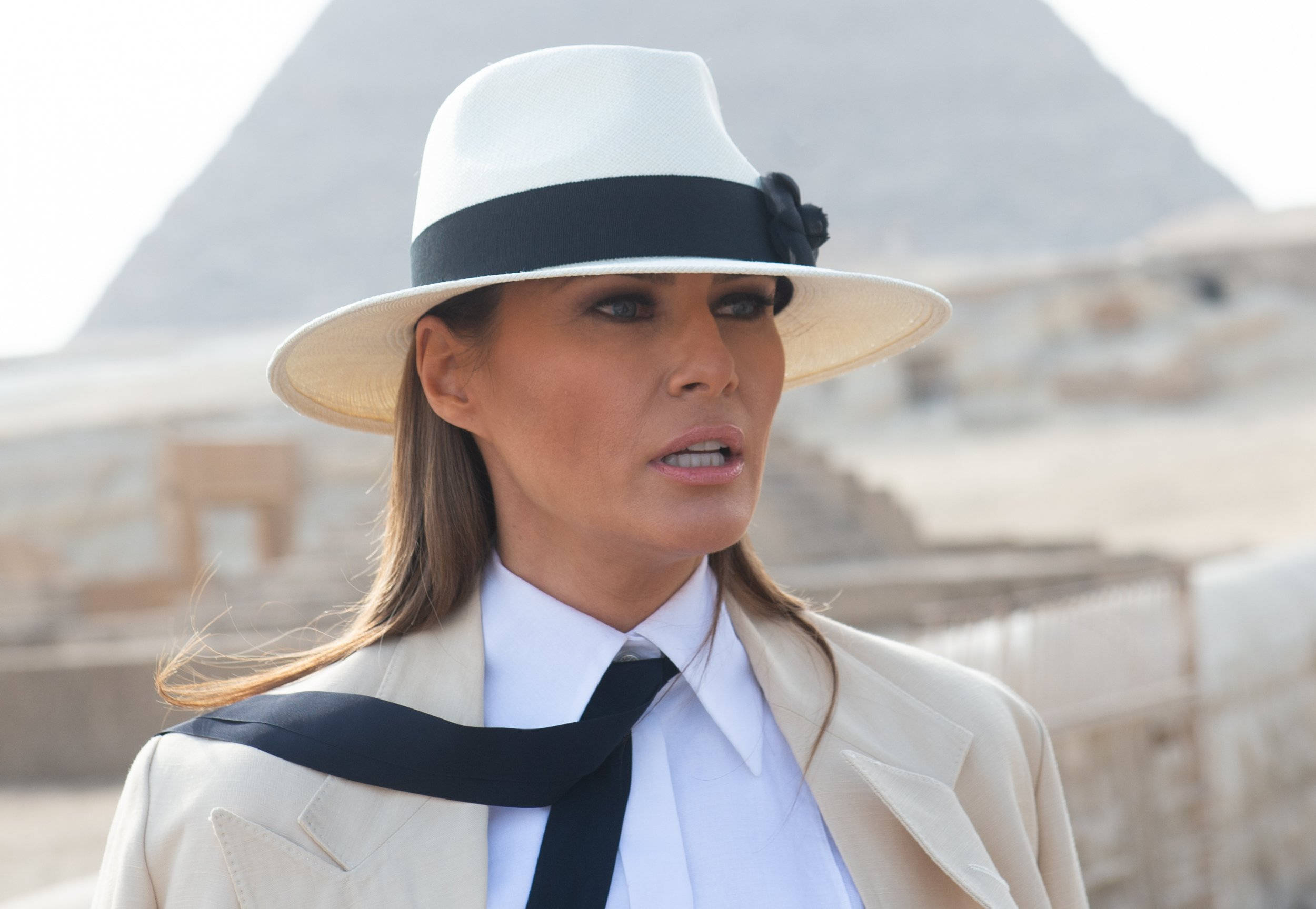 Melania 桌布 壁紙 — 一位戴白色帽子和穿米色外套的女性站在明亮的沙漠天空下，背景是標誌性的吉薩金字塔。