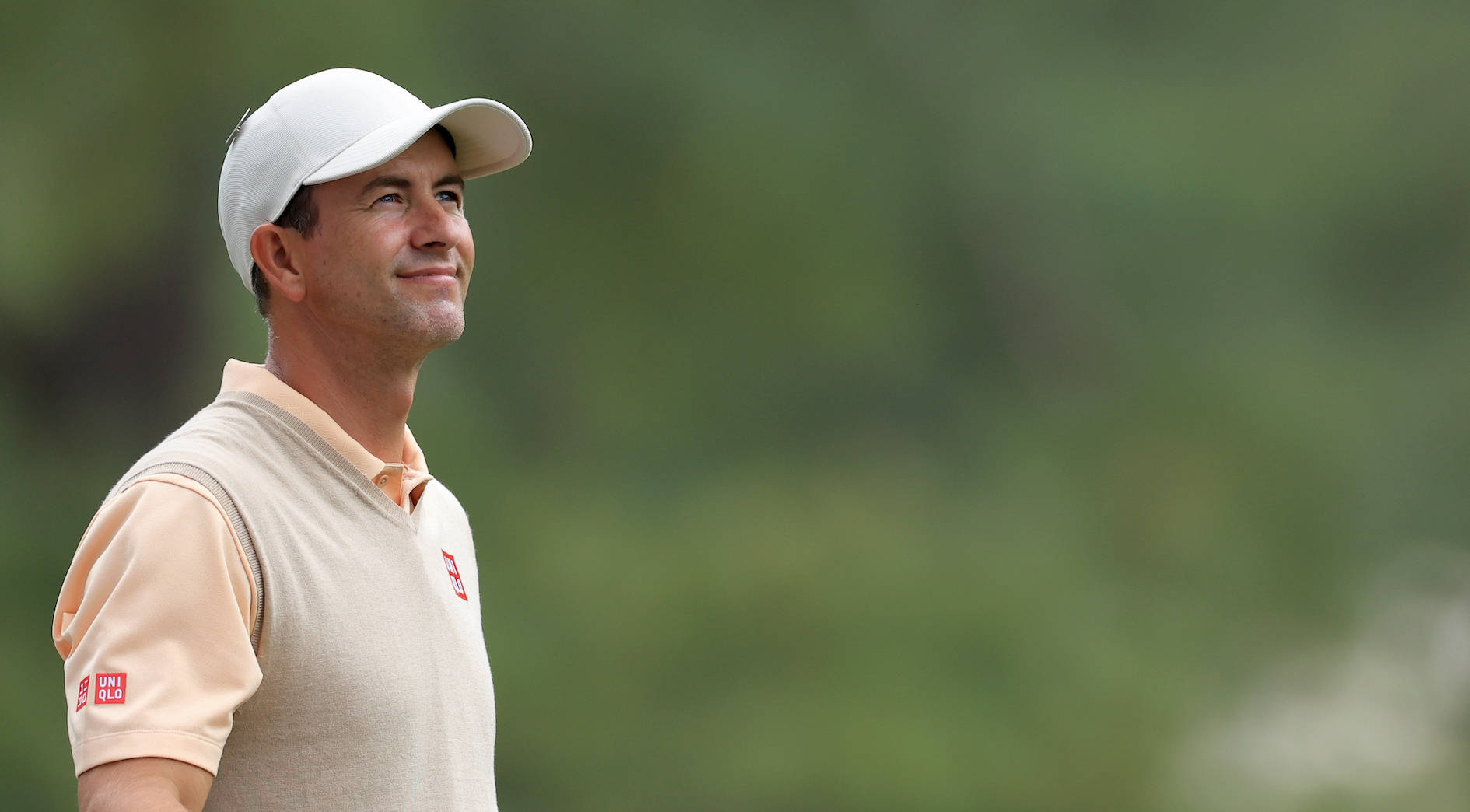 adam scott 桌布 壁紙 — 一位戴白色帽子和米色背心的高爾夫球手在柔和的綠色模糊背景下自信地微笑。