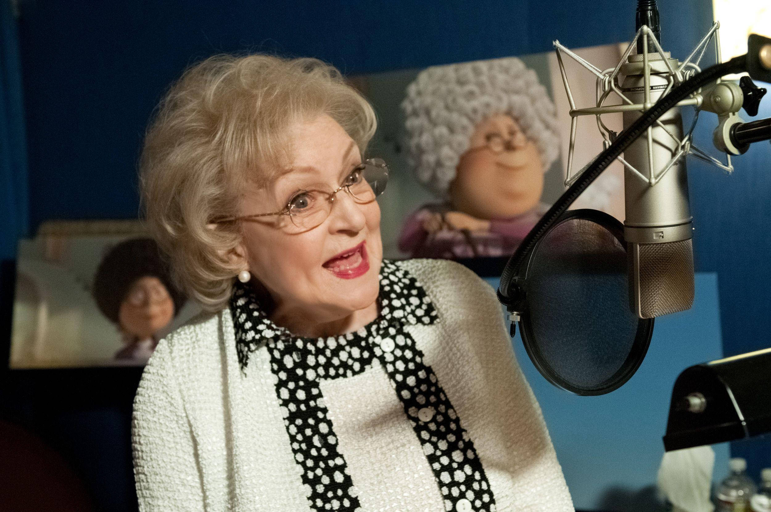 Betty White 桌布 壁紙 — 一位戴眼鏡、捲髮的老年女性在錄音室裡微笑著錄音，身後有麥克風和木偶海報。