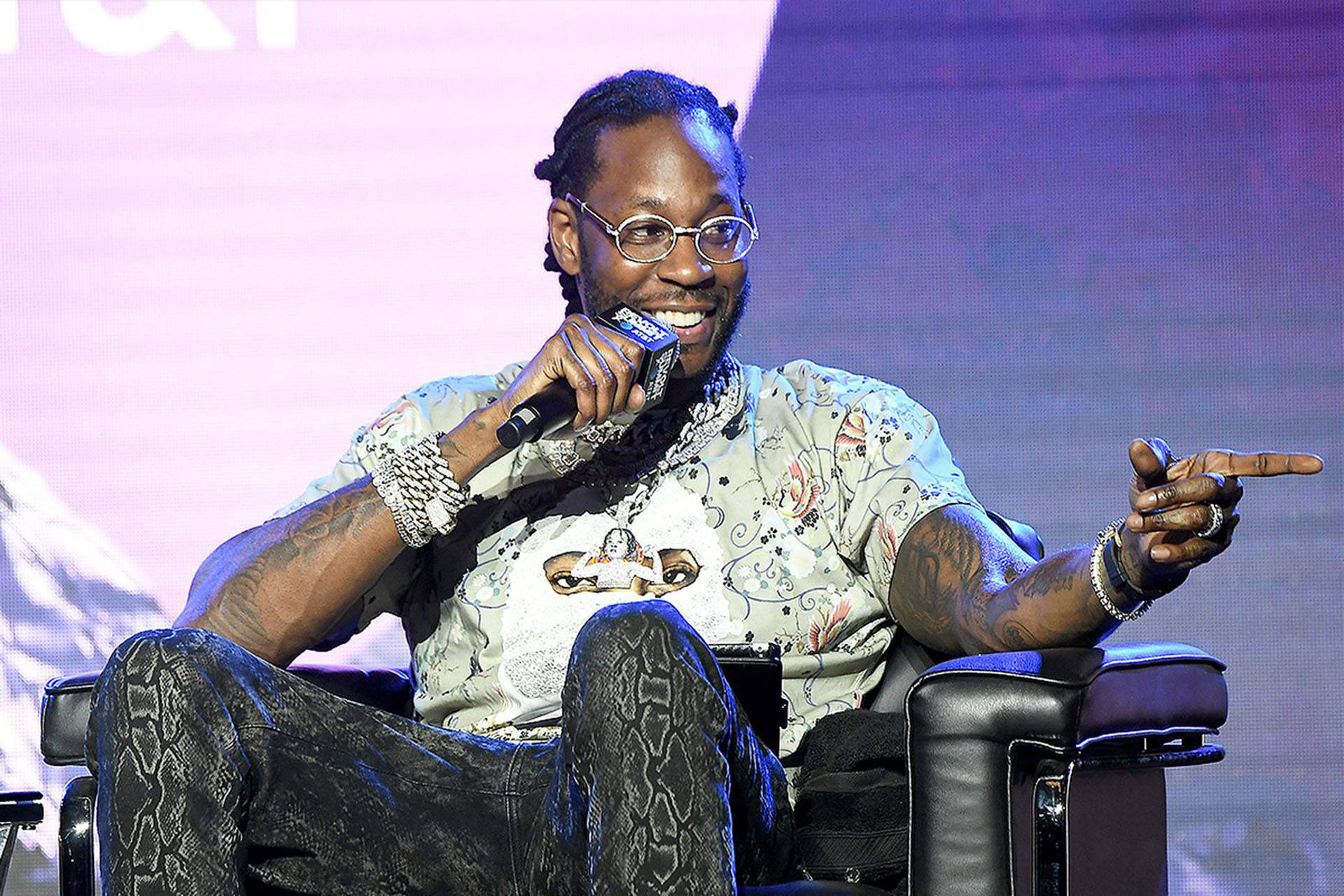 2 Chainz 桌布 壁紙 — 一位戴眼鏡、有刺青的微笑男子在燈光明亮的舞台上手持麥克風比手勢。