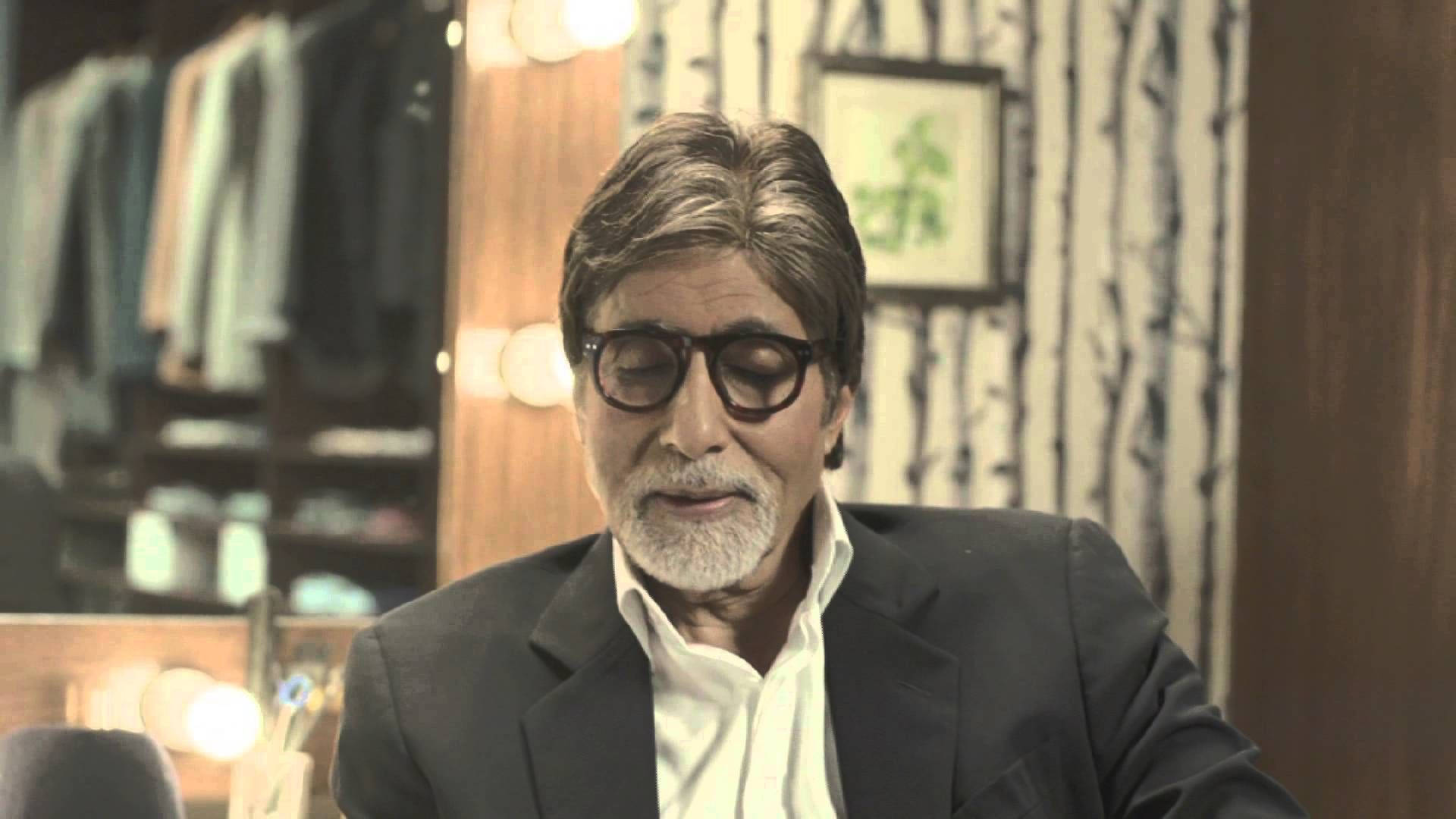 Amitabh Bachchan 桌布 壁紙 — 一位戴眼鏡、留白鬍子的尊貴長者坐在一個光線溫暖、有木架和圖案壁紙的房間裡。