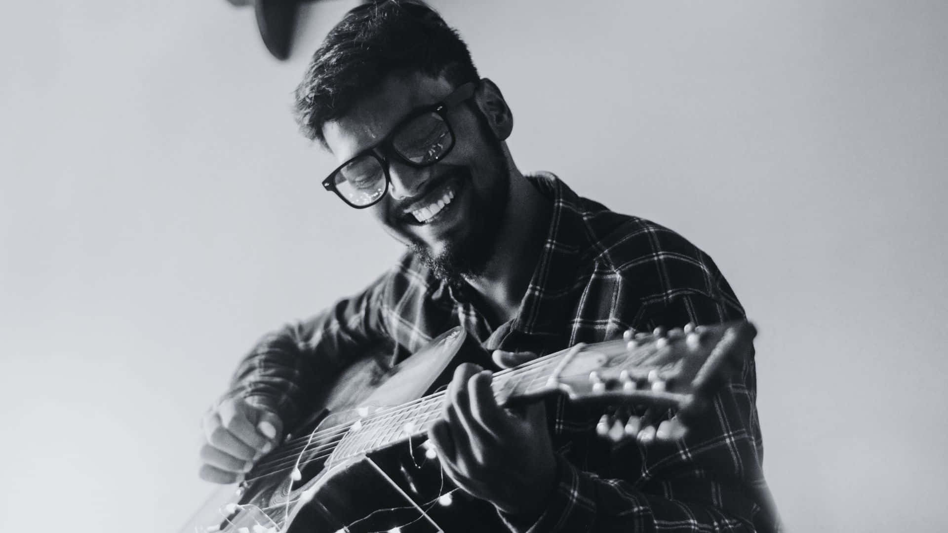 Black And White Guitar 桌布 壁紙 — 一位戴眼鏡、留鬍子的快樂男士，在黑白工作室照中微笑彈奏木吉他。