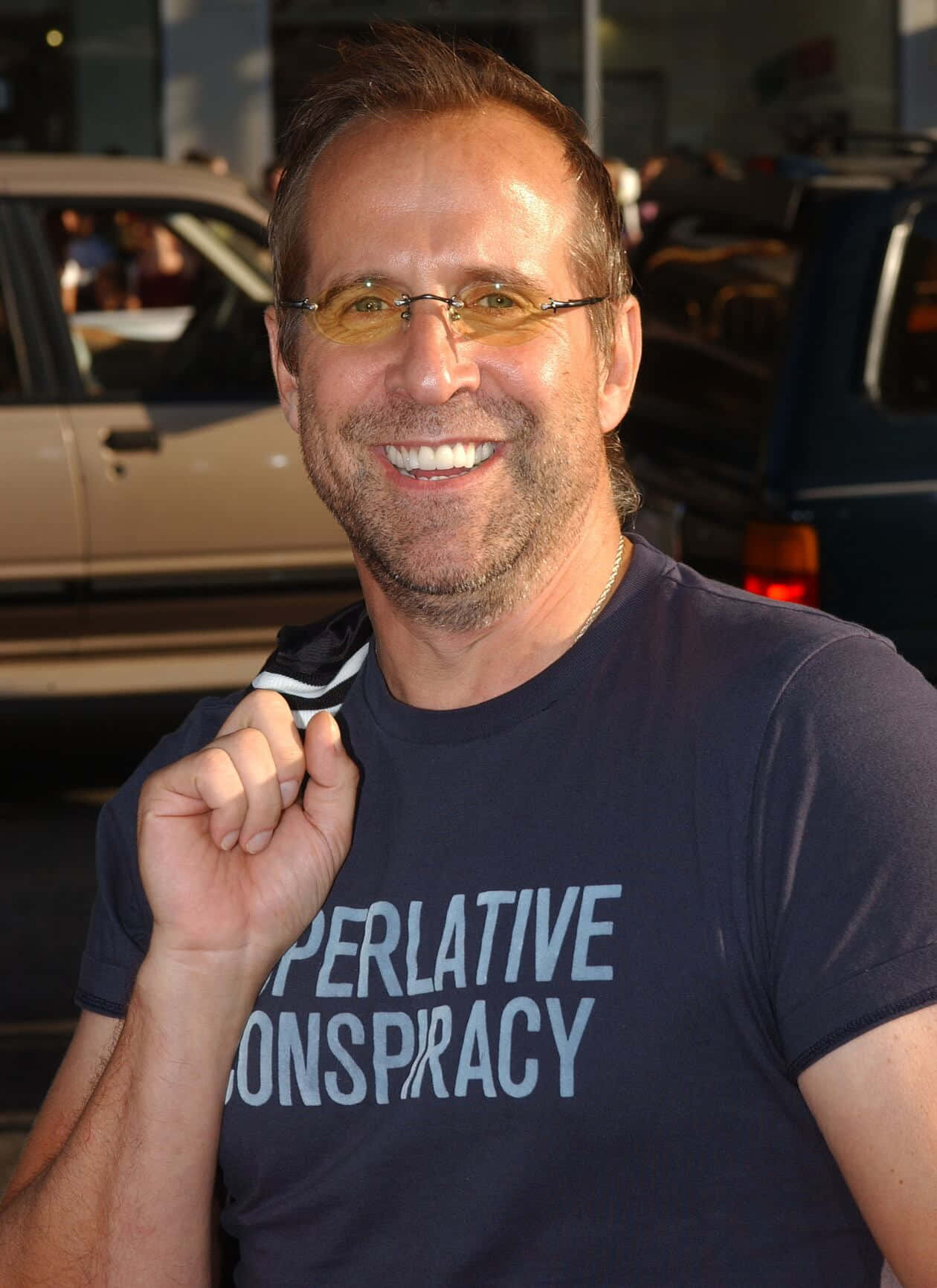 Peter Stormare 桌布 壁紙 — 一位戴眼鏡、留鬍渣的男士面帶微笑，身穿印有 'OPERATIVE CONSPIRACY' 字樣的深色T恤，在戶外靠近汽車的地方擺姿勢。