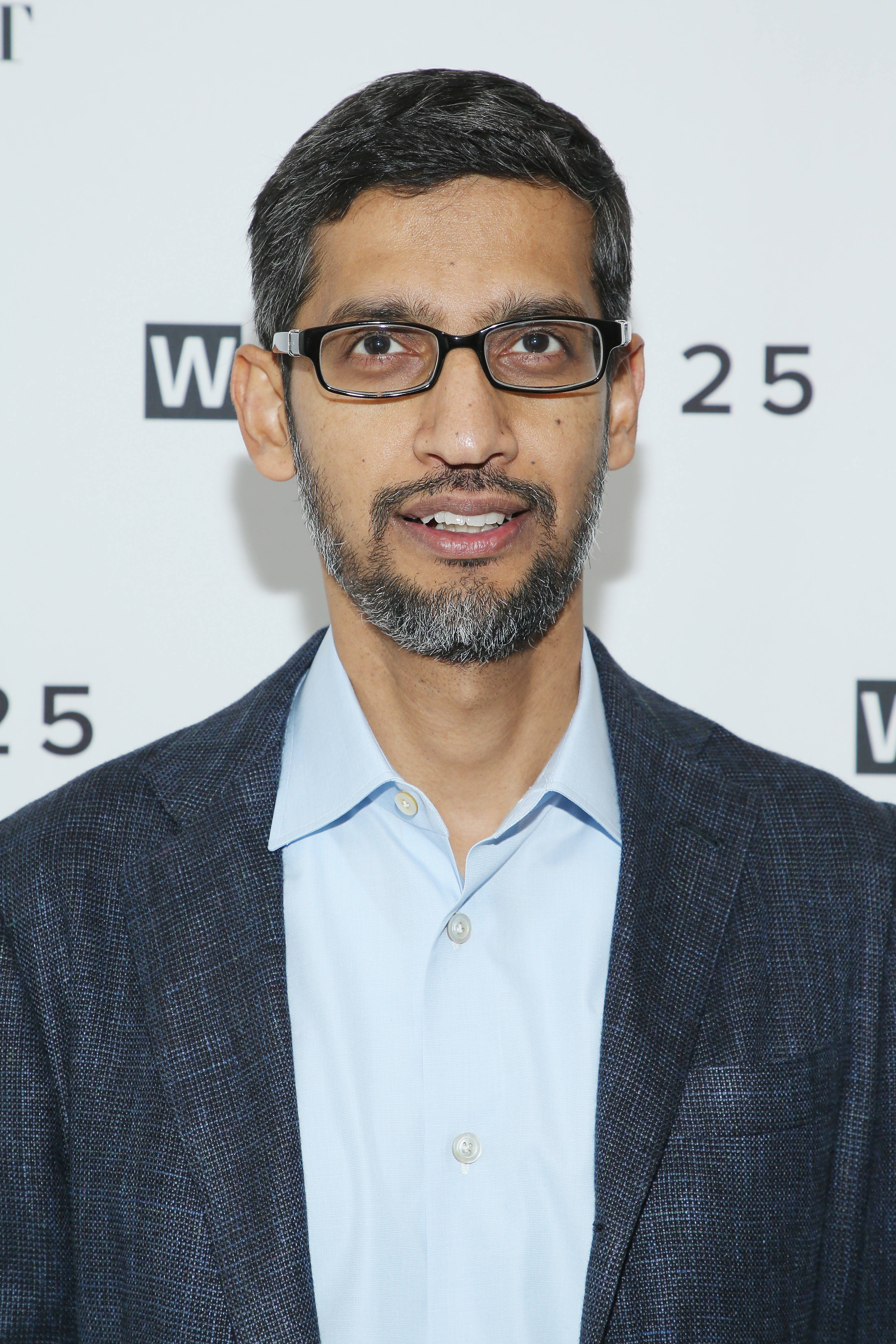 google 桌布 壁紙 — 一位戴眼鏡、留鬍鬚的男子，身穿深色西裝外套，內搭淺藍色襯衫，背景為白色，帶有「W25」標誌。