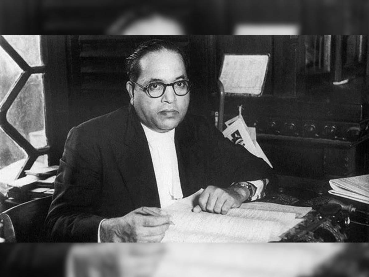 Dr Babasaheb Ambedkar 桌布 壁紙 — 一位戴眼鏡、穿著正裝的嚴肅男子坐在雜亂的辦公桌前，在燈光昏暗的辦公室裡審閱文件。
