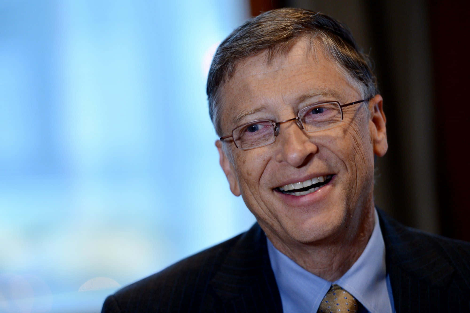 Bill Gates 桌布 壁紙 — 一位戴眼鏡、穿著西裝打領帶的男士在模糊背景前的微笑特寫肖像。