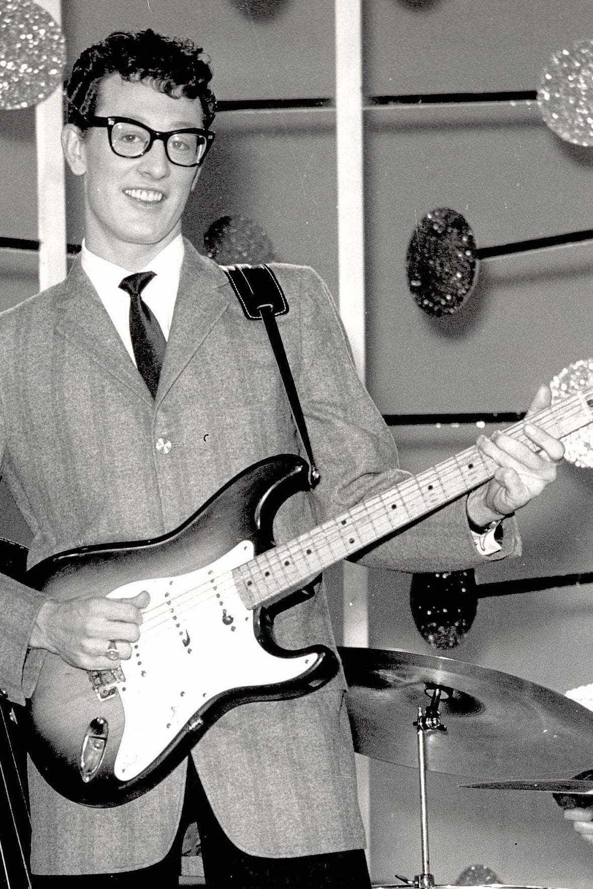 Smile 桌布 壁紙 — 一位戴眼鏡、穿西裝的微笑男士在舞台上演奏 Fender Stratocaster 吉他，舞台上有閃爍的迪斯可球和鼓組。
