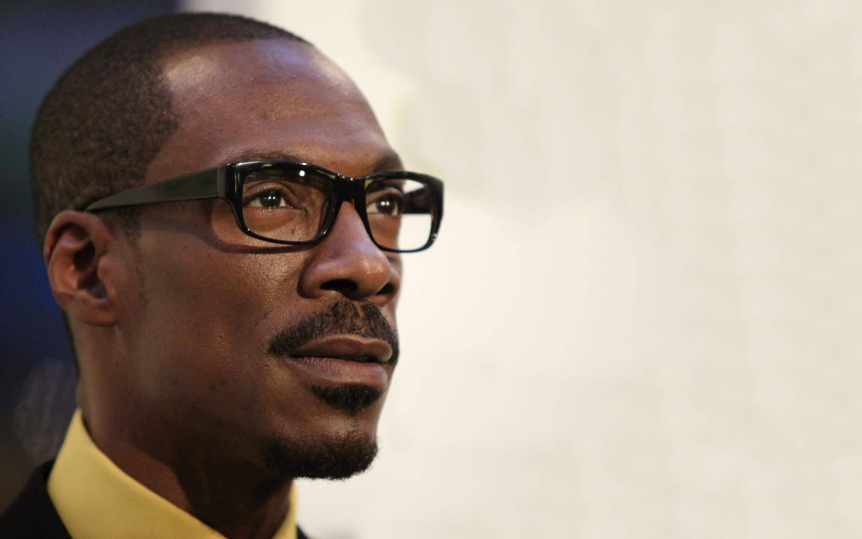 eddie murphy 桌布 壁紙 — 一位戴眼鏡、穿黃色領子的男士若有所思地望向一邊的特寫肖像。