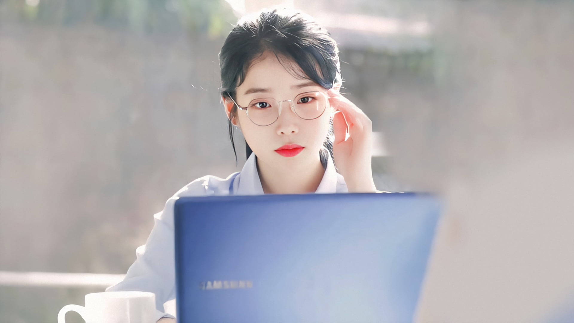 Kpop Aesthetic 桌布 壁紙 — 一位戴眼鏡、紅唇的年輕女性專注地看著她的筆記型電腦，陽光從她身後的窗戶照射進來。