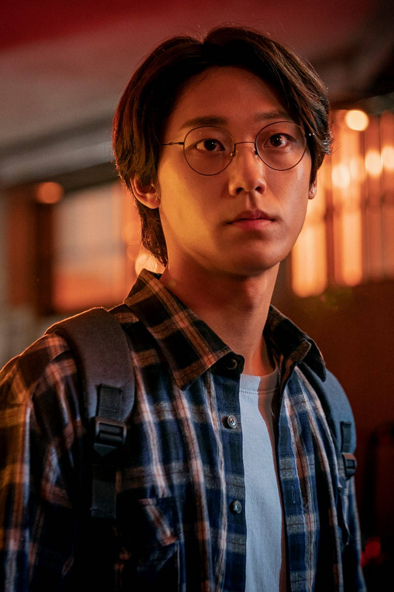 Sweet Home Netflix 桌布 壁紙 — 一位戴眼鏡、身穿格紋襯衫的年輕男子，在溫暖的環境燈光下凝視著相機。