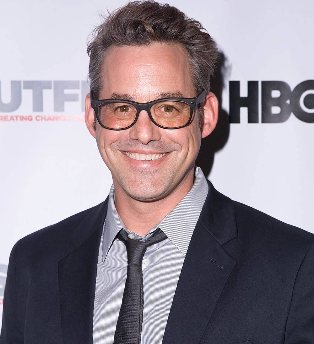 Nicholas Brendon 桌布 壁紙 — 一位戴眼鏡、身穿深色西裝的微笑男士，在帶有HBO和Outfit7標誌的白色背景前擺姿勢。