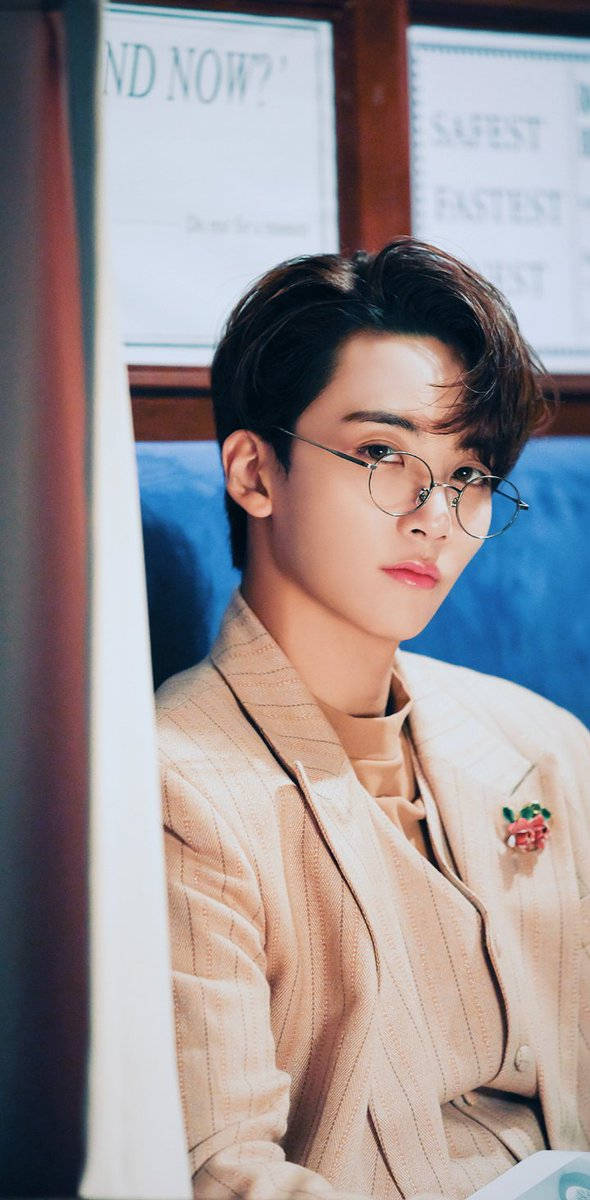 yoon jeonghan 桌布 壁紙 — 一位戴眼鏡、身穿米色西裝的年輕男子，在溫暖照明的室內環境中，若有所思地坐在藍色沙發上。