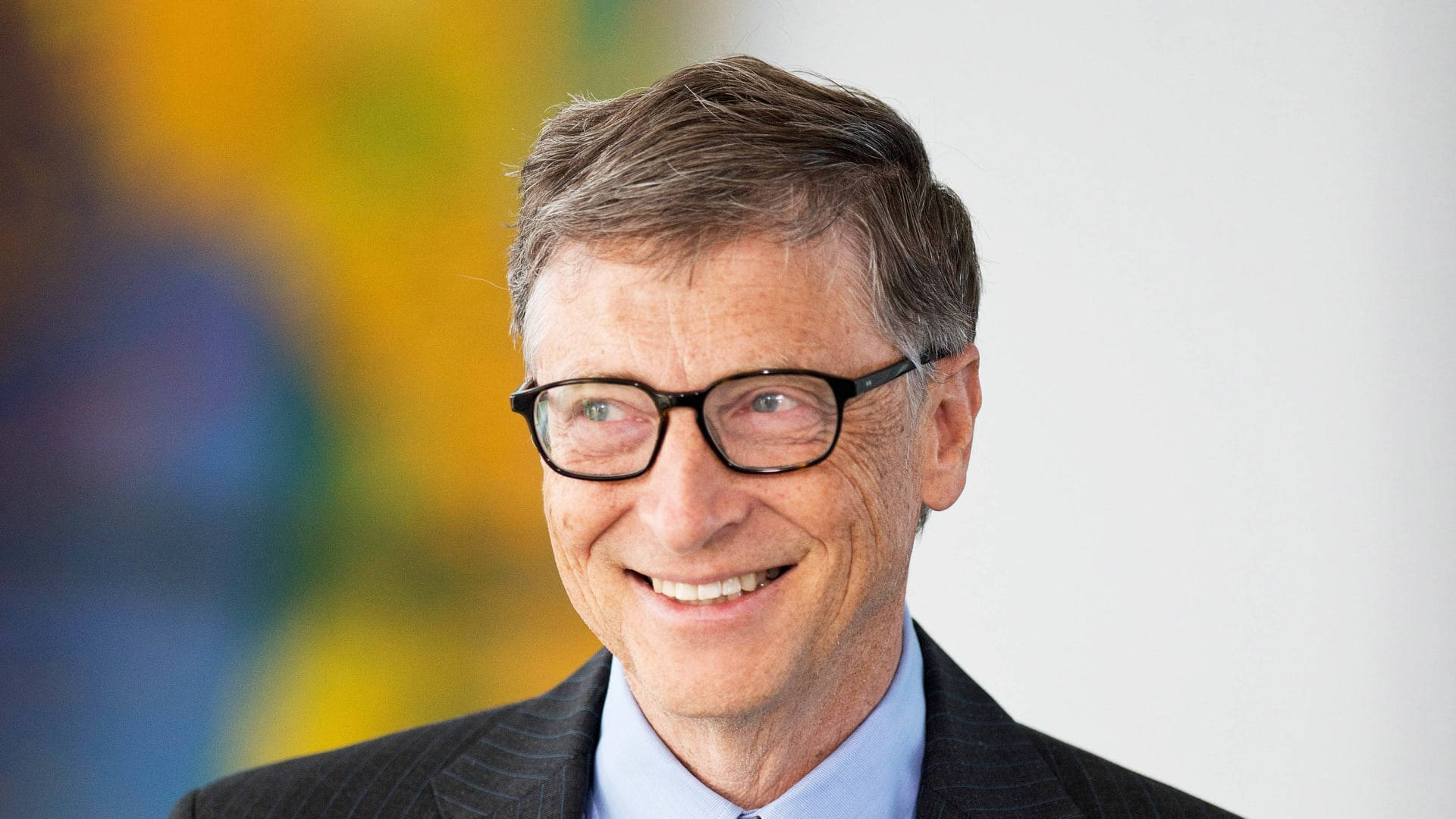 gates 桌布 壁紙 — 一位戴眼鏡、身穿西裝、微笑的男士的特寫肖像，背景是色彩繽紛的模糊效果。
