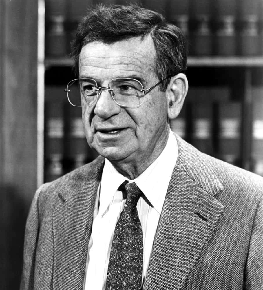Walter Matthau 桌布 壁紙 — 一位戴眼鏡、身穿西裝及圖案領帶的長者站在書架前的黑白肖像。