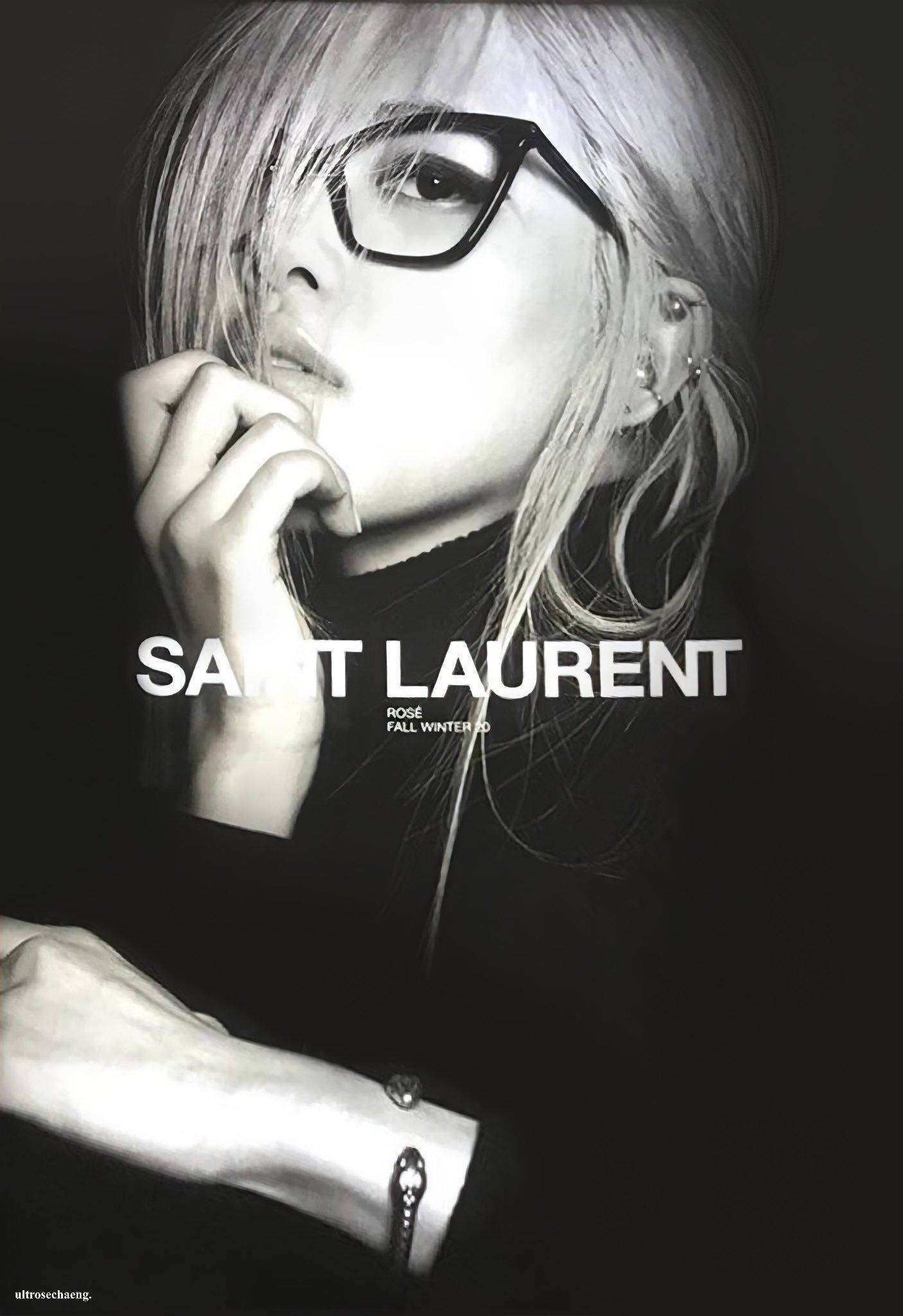 Sunglasses 桌布 壁紙 — 一位戴眼鏡、金髮的女性，手靠近嘴邊，穿著 Saint Laurent 服裝的黑白肖像。