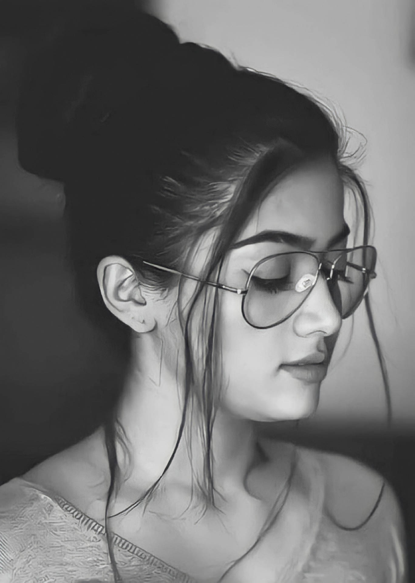 一位戴眼鏡、頭髮盤成髮髻的女性，閉著眼睛，黑白。 — 拉什米卡·曼丹娜 壁紙