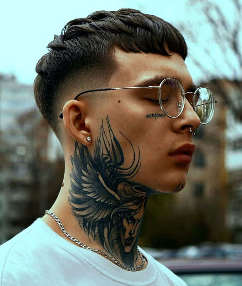 Face Tattoo 桌布 壁紙 — 一位戴眼鏡、頸上有大型天使翼刺青的年輕男子，在都市環境中閉眼站立。