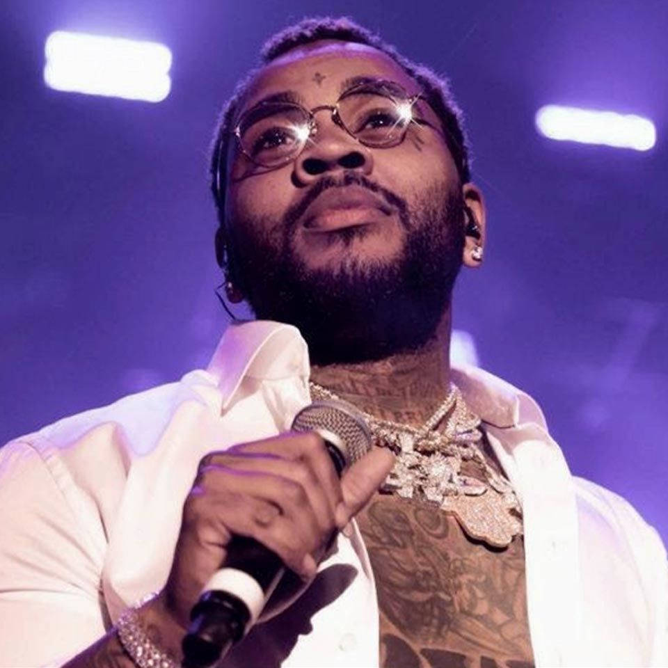 Kevin Gates 桌布 壁紙 — 一位戴眼鏡及有刺青的男饒舌歌手在紫色燈光下手持麥克風於舞台上表演。