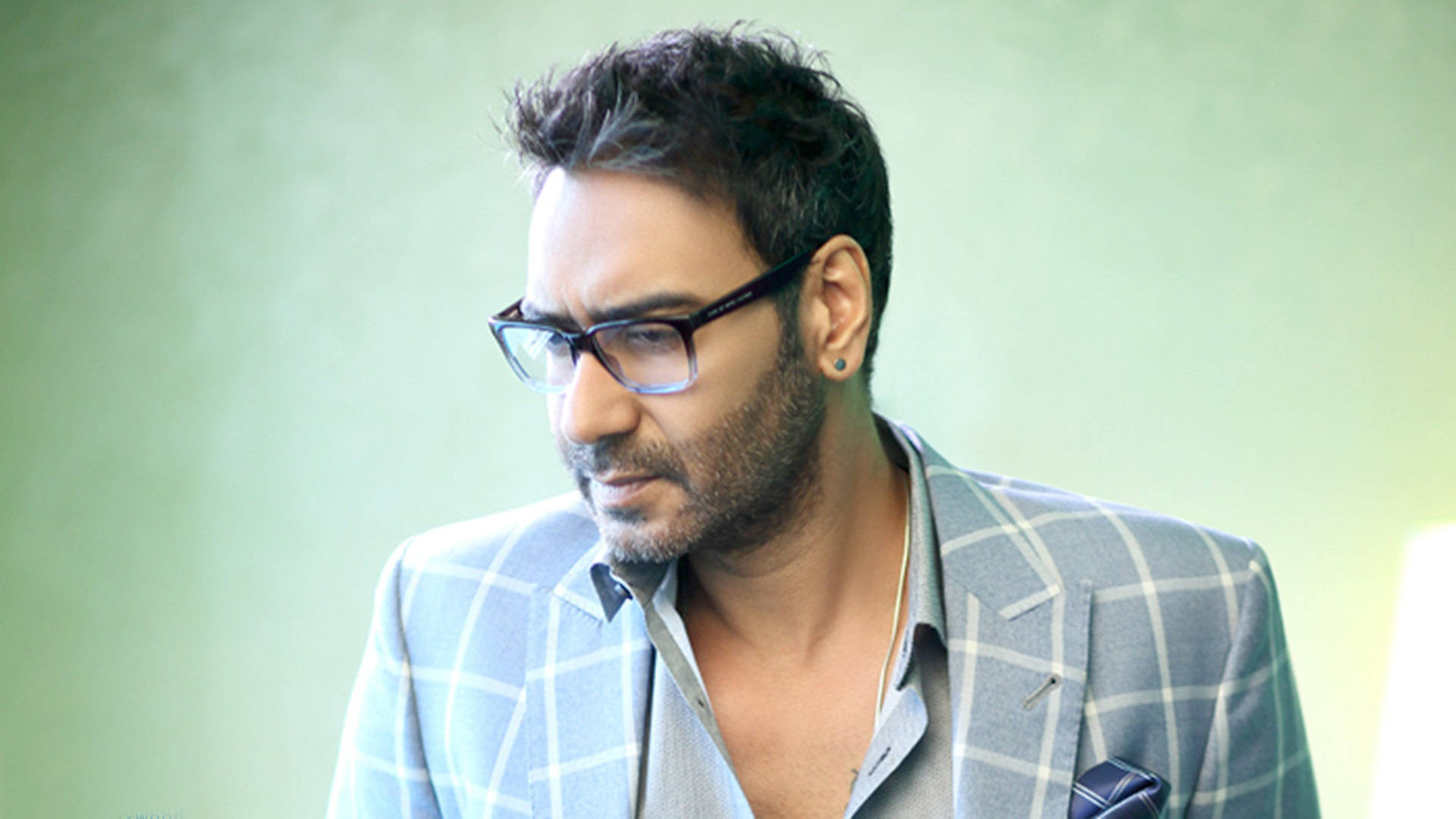 ajay devgn 桌布 壁紙 — 一位戴眼鏡和格紋西裝外套的男人在柔和的綠色背景下若有所思地凝視。
