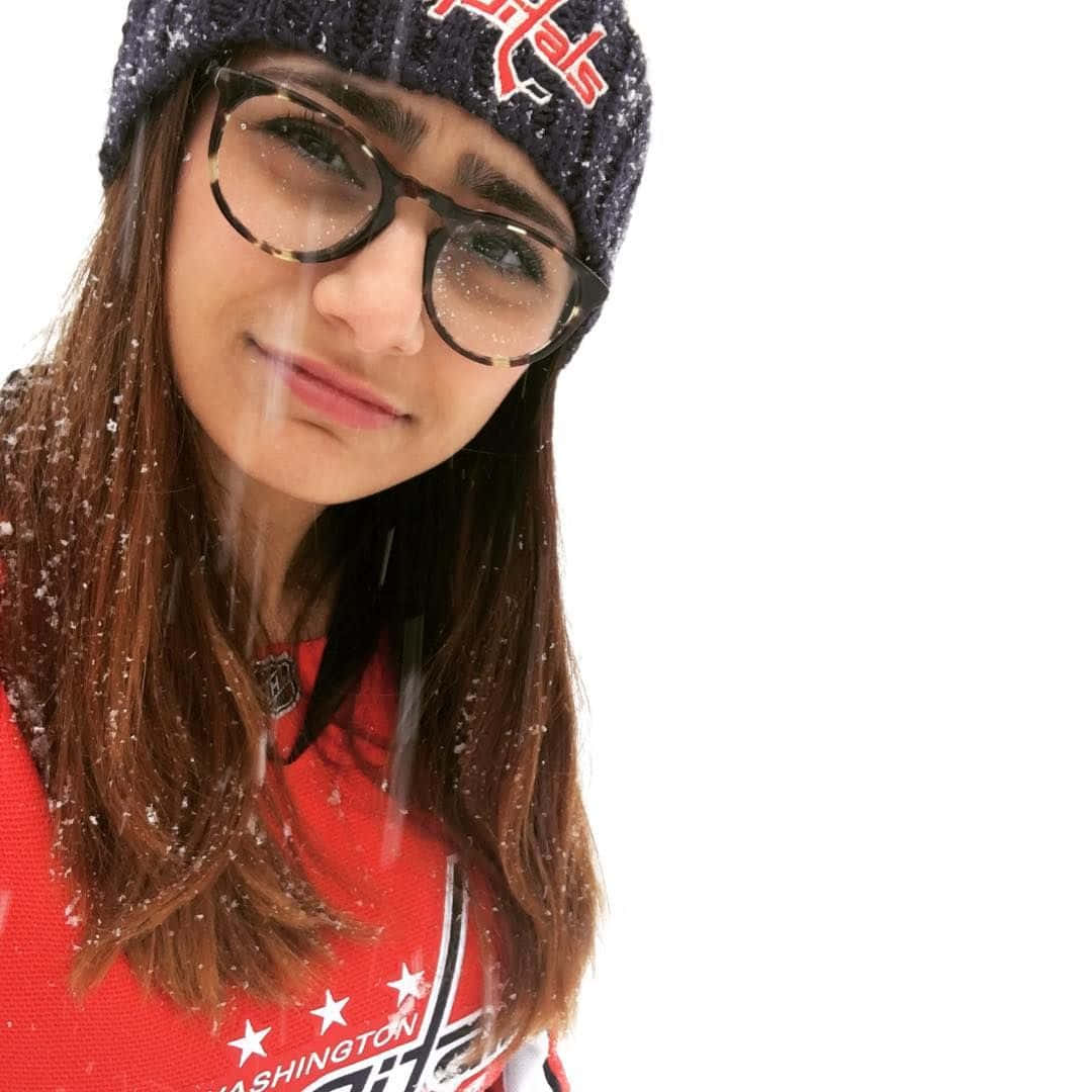 Mia Khalifa 桌布 壁紙 — 一位戴眼鏡和毛帽的年輕女性在明亮的冬日場景中，雪花飄舞，她溫柔地微笑。